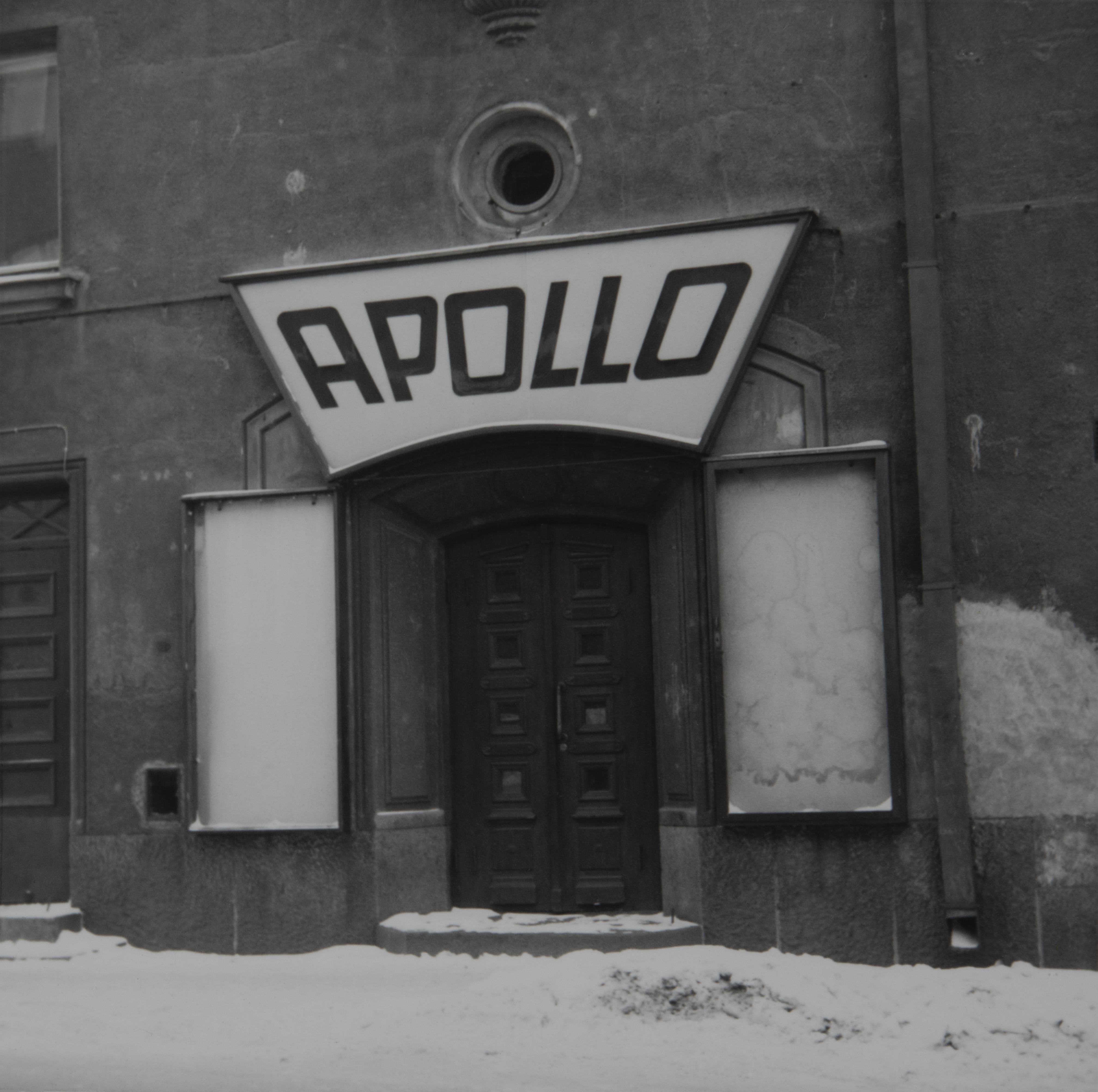 Näkymä elokuvateatteri Apollon sisäänkäynnistä ulkopuolelta, Hämeentie 78. Teatteri lopetti toimintansa joulukuussa 1965 ja vuonna 1966 se purettiin. Sisäänkäynnin molemmin puolin ovat mainoksia varten vitriinit, ja sisäänkäynnin yläpuolella teatterin nimen kertova valomainos.