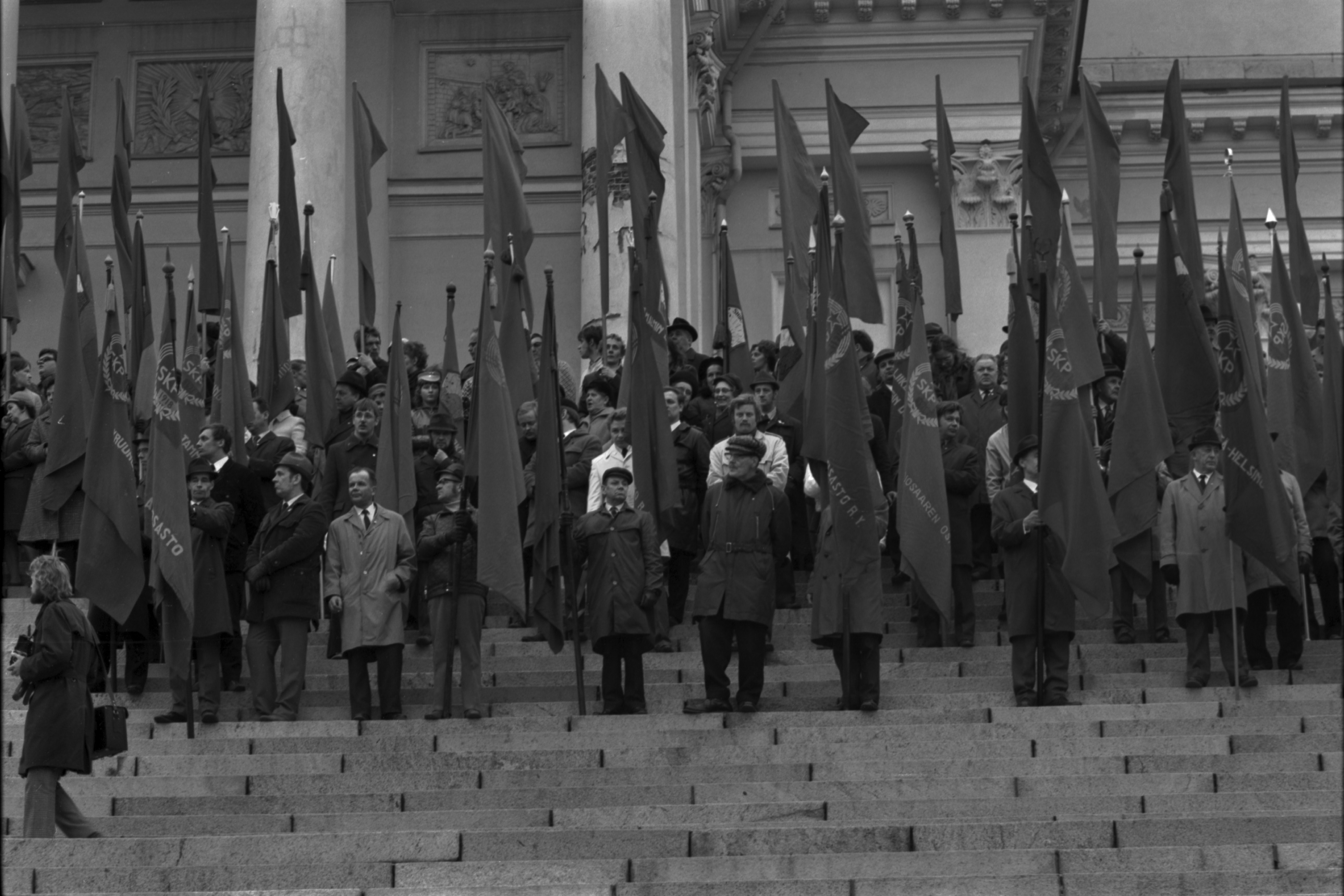 Hallituskatu 7. Työväen vappujuhlaan osallistuvia ihmisiä lippuineen Tuomiokirkon portailla 1.5.1972.