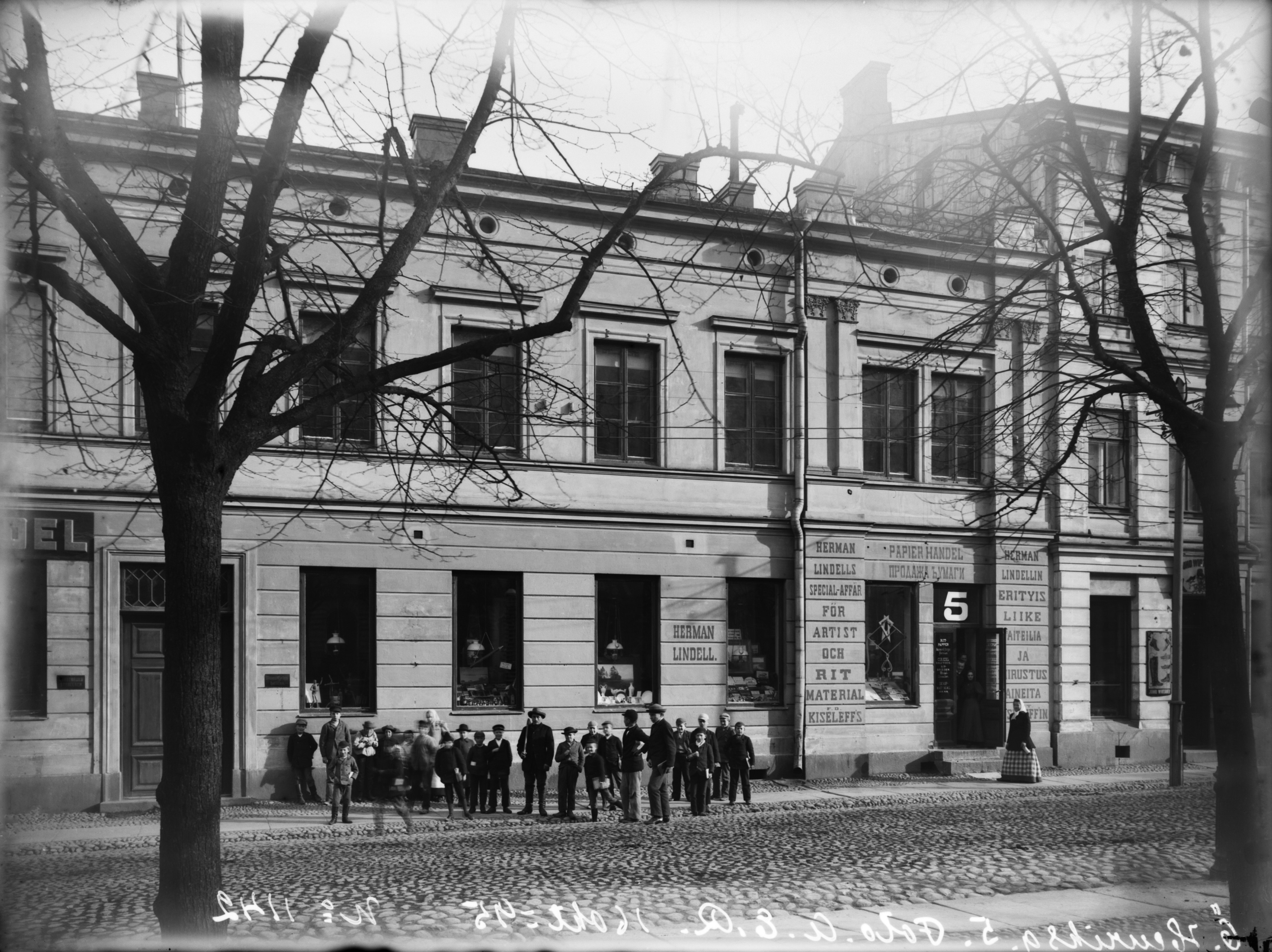 Ryhmä lapsia Itäinen Heikinkatu 5:n (=Mannerheimintie 1) edessä, taustalla Herman Lindellin taiteilija- ja piirustusvälineitä myyvä paperikauppa.
