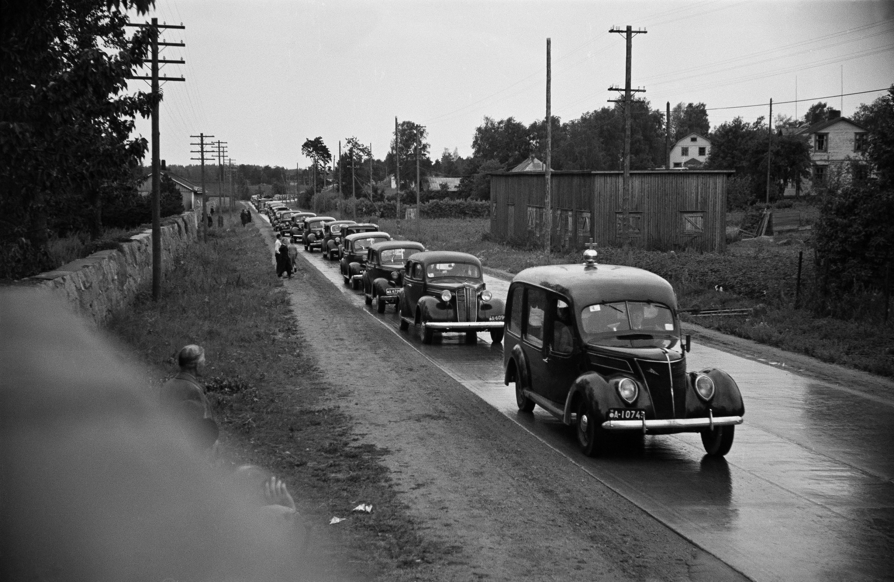 Hautasaatto saapumassa Pohjoiselle hautausmaalle (=Malmin hautausmaa). Etummainen auto Ford vm. 1937. Sen takana Dodge vm. 1937.