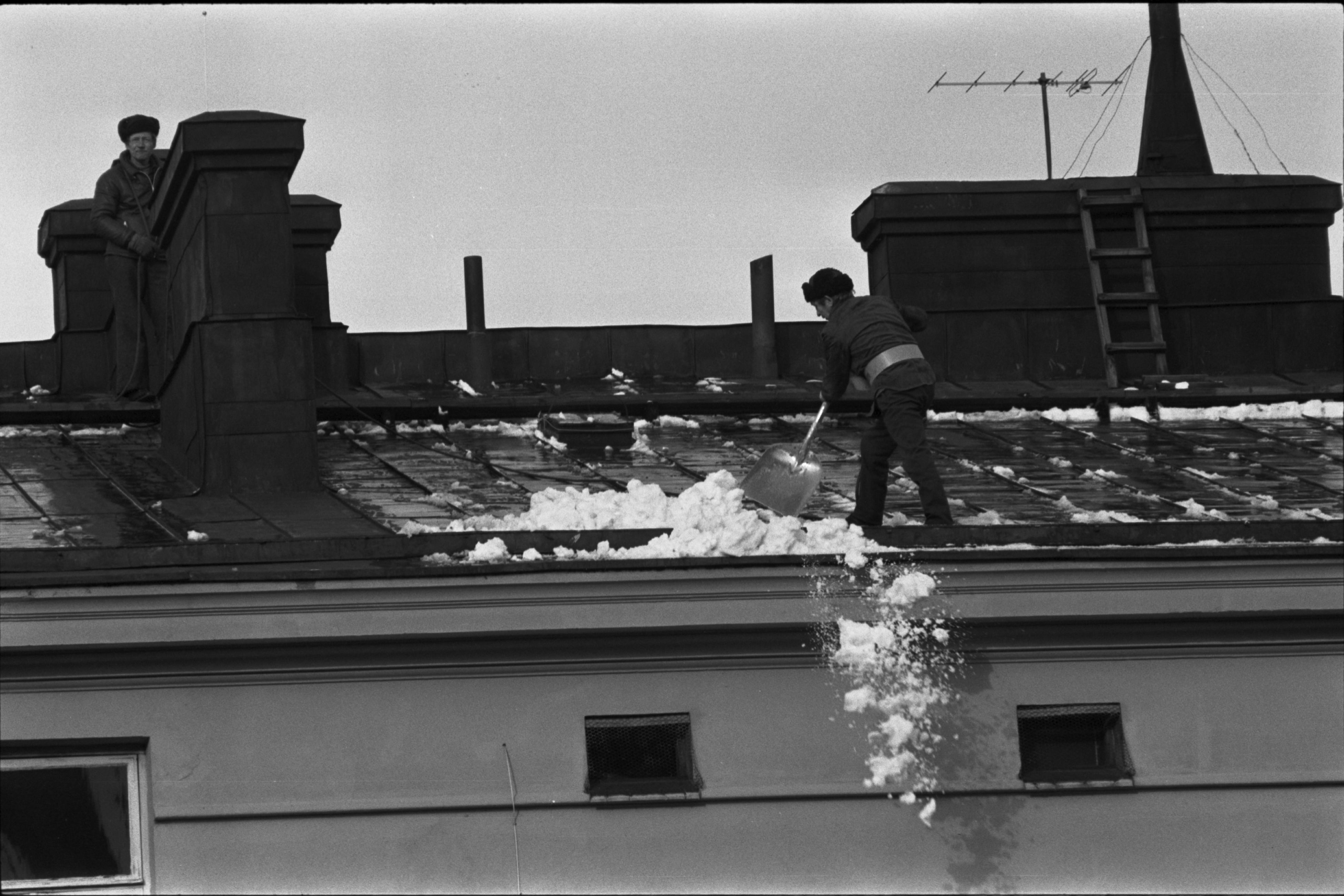 Liisankatu 7. Kaksi miestä pudottamassa lunta Liisankatu 7:n talon pihan puolen katolta.