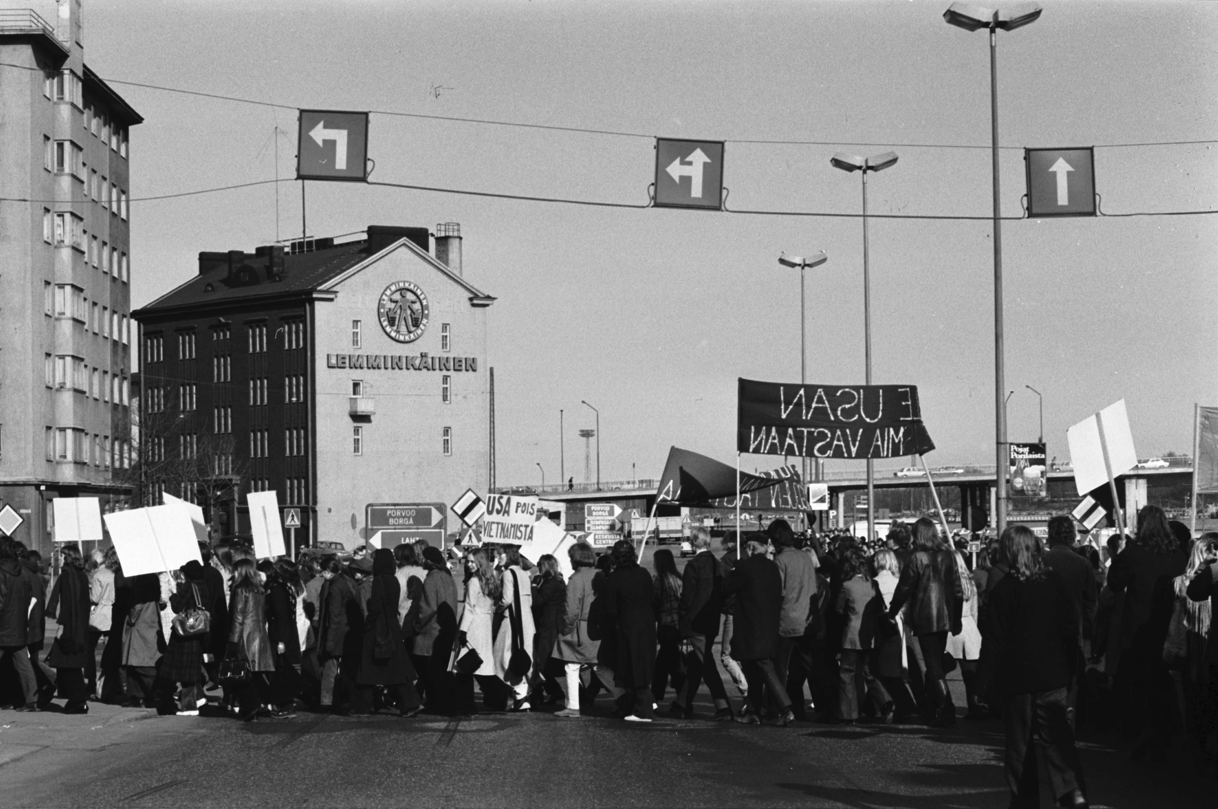Vietnamin sodan vastainen mielenosoituskulkue plakaatteineen ja banderolleineen Hakaniemenrannassa kääntymässä Hakaniementorille. Taustalla Lemminkäisen talo.