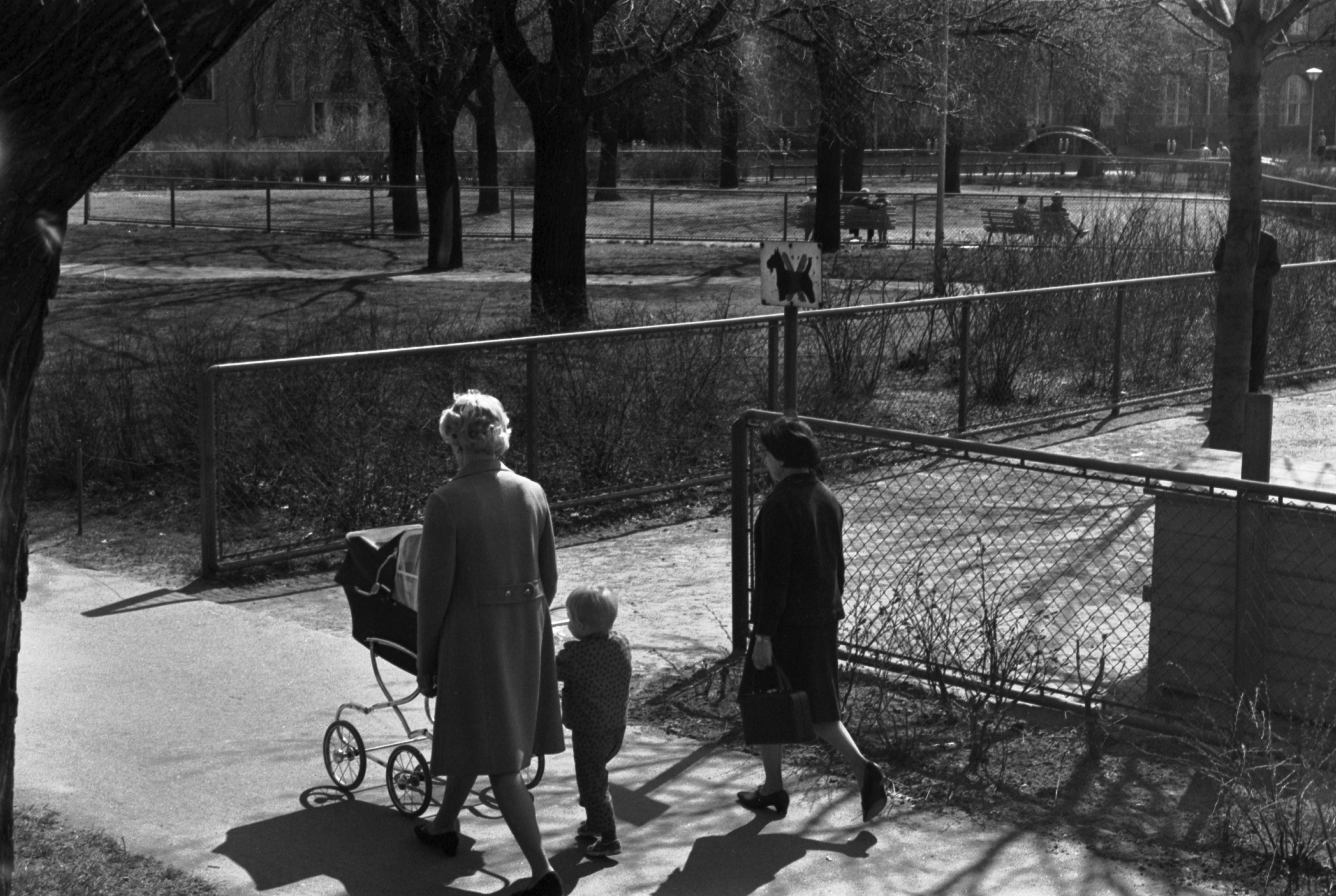 Eläintarhantie. Näkymä Eläintarhantien suunnalta keväiseen Eläintarhanlahden pohjukassa olevaan puistoon. Etualalla kaksi naista ja lapsi kävelemässä lastenvaunujen kanssa. Taustalla Säästöpankinrantaa.