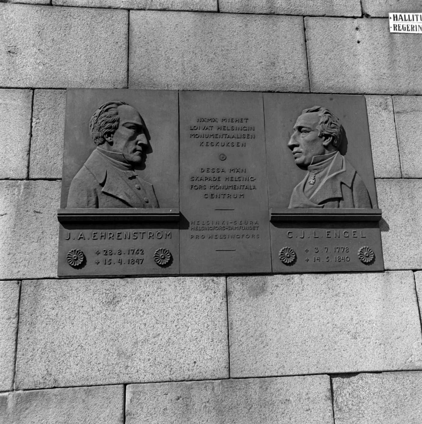 Empire-Helsingin suunnittelijoiden J. A. Ehrenströmin ja C. L. Engelin muistolatta Yliopiston kirjaston muurissa, Hallituskatu 9 (= Yliopistonkatu 1).