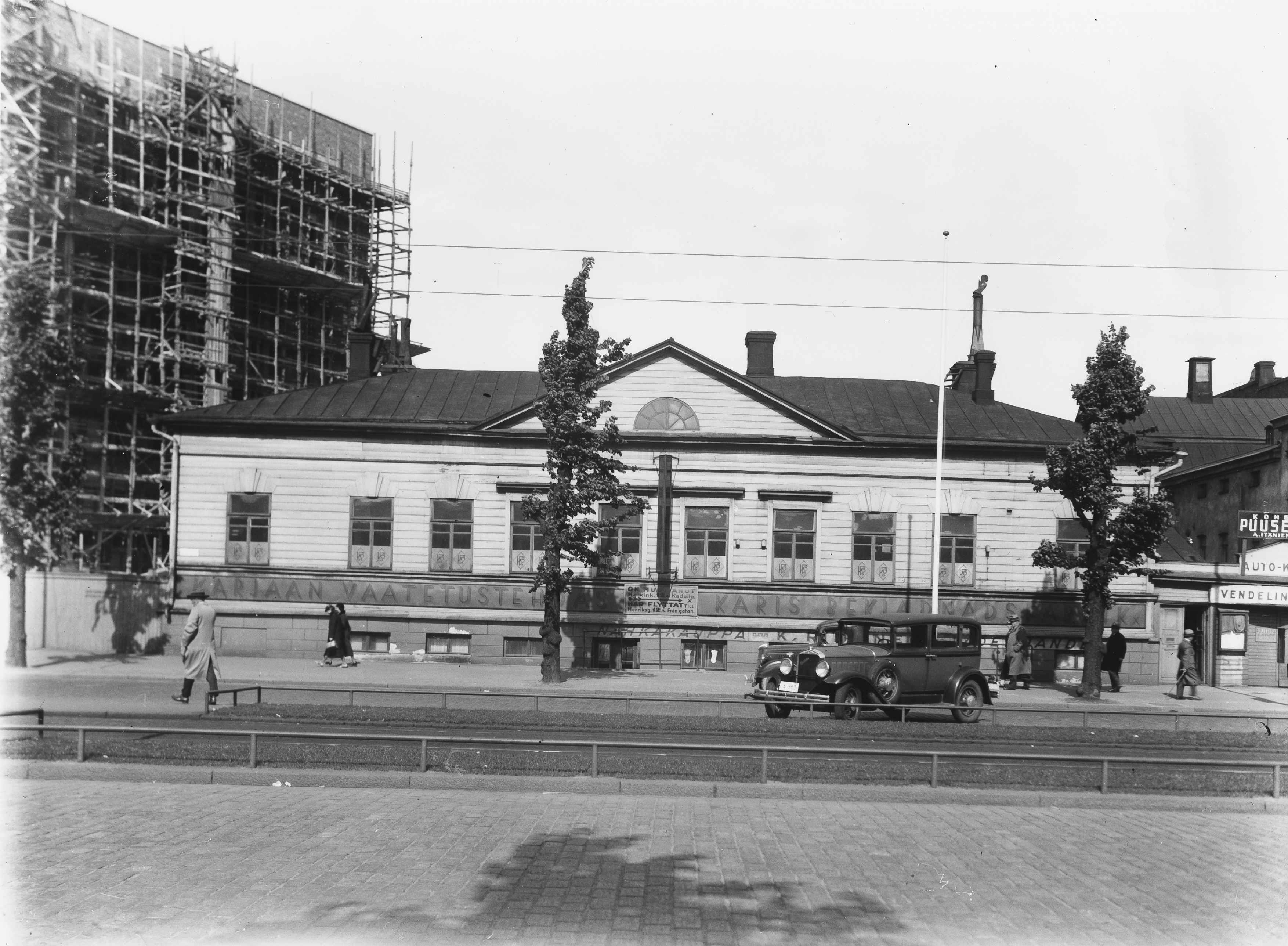 Heikinkatu 15 (=Mannerheimintie 9). Talon kyljessä lukee Karjaan vaatetustehdas.  Postitalon rakentaminen vasemmalla.