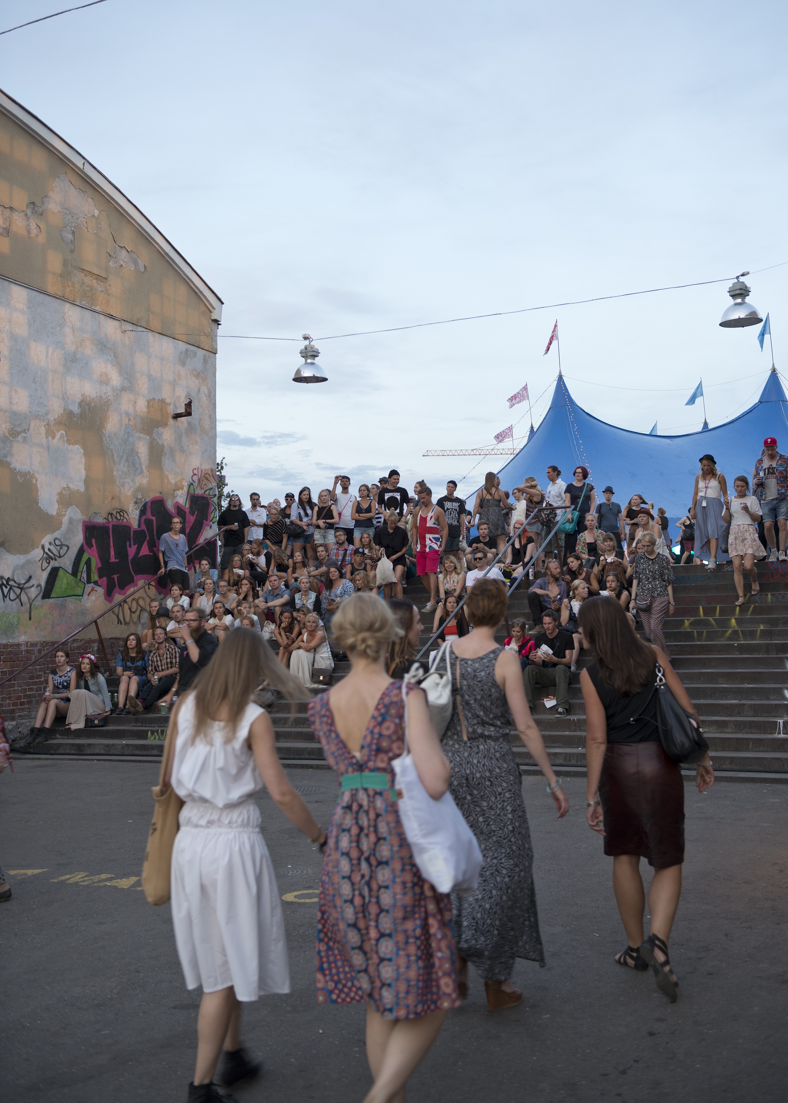 Flow Festival. Flow Festivalin kävijöitä Mittarikorjaamon ja Valvomon välissä olevilla portailla odottamassa festivaalin päätöspäivän pääesiintyjän keikan alkamista. Taustalla oikealla Lumia Blue Tent, yksi festivaalin yhdeksästä esiintymisalueesta.