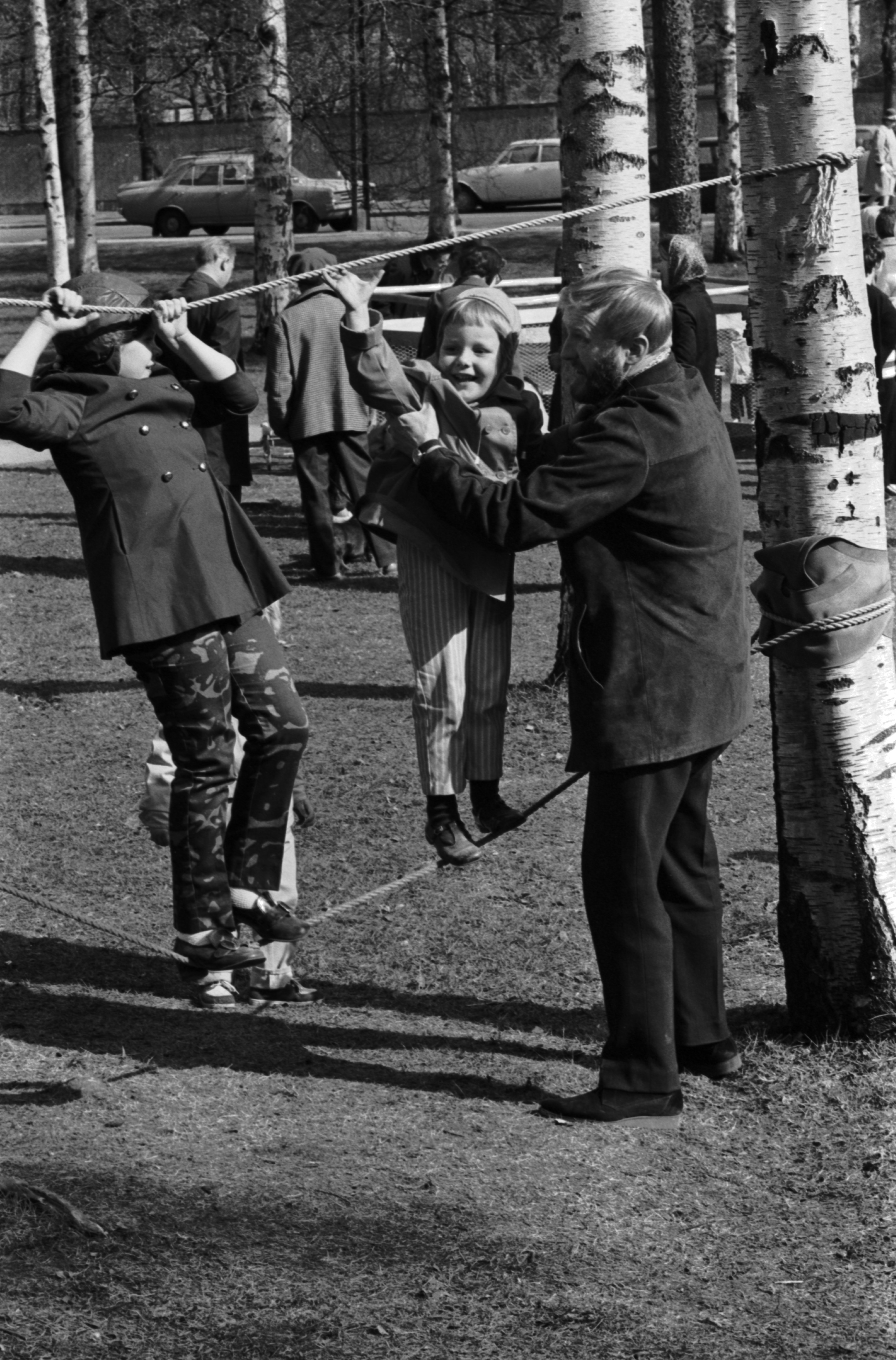 Sibeliuksen puisto. Helsingin juhlaviikot. Mies auttaa puiden väliin pingotetuilla köysillä kiipeilevää tyttöä Sibeliuksen puistossa järjestetyssä puistotapahtumassa.