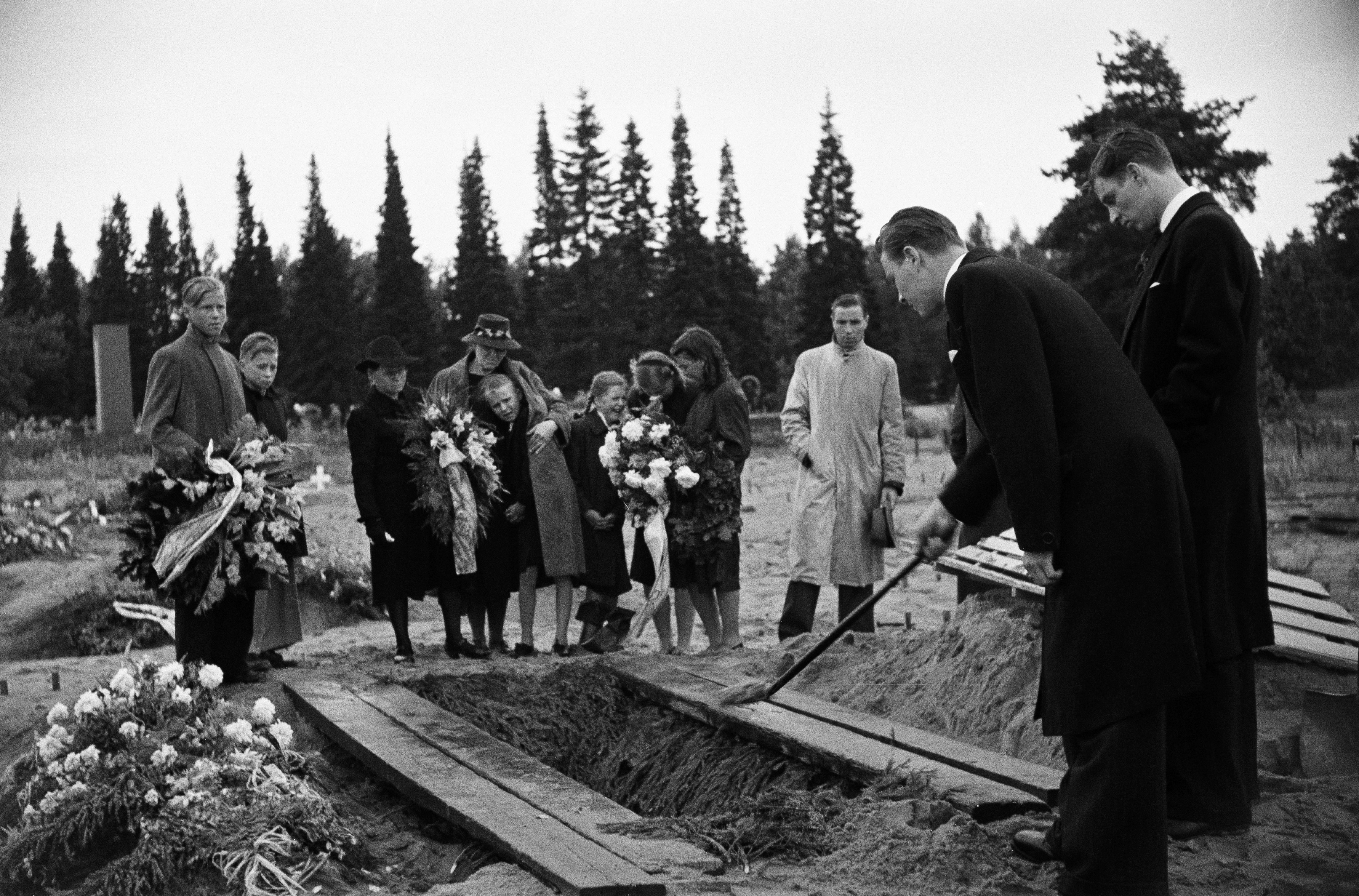 Hautajaiset Pohjoisella hautausmaalla (=Malmin hautausmaa), mies heittää arkulle hiekkaa.