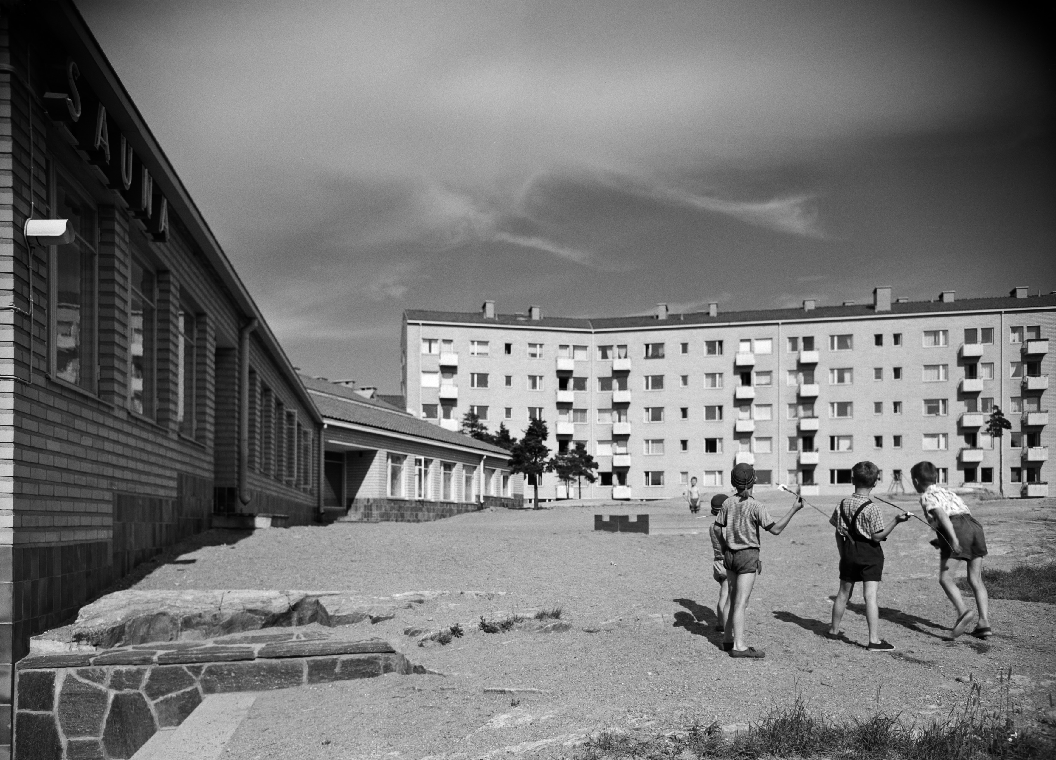 Mannerheimintie 93 / Lehtikuusentie 2. Asuntoyhteistalo Oy. Rakennuksen on suunnitellut Olli Saijonmaa, valmistunut 1953. Pojat leikkivät keihäänheittoa rakennuksen pihalla. Kuva on otettu pihan pohjoisosasta koilliseen päin. Vasemmalla olevassa piharakennuksessa on sauna.