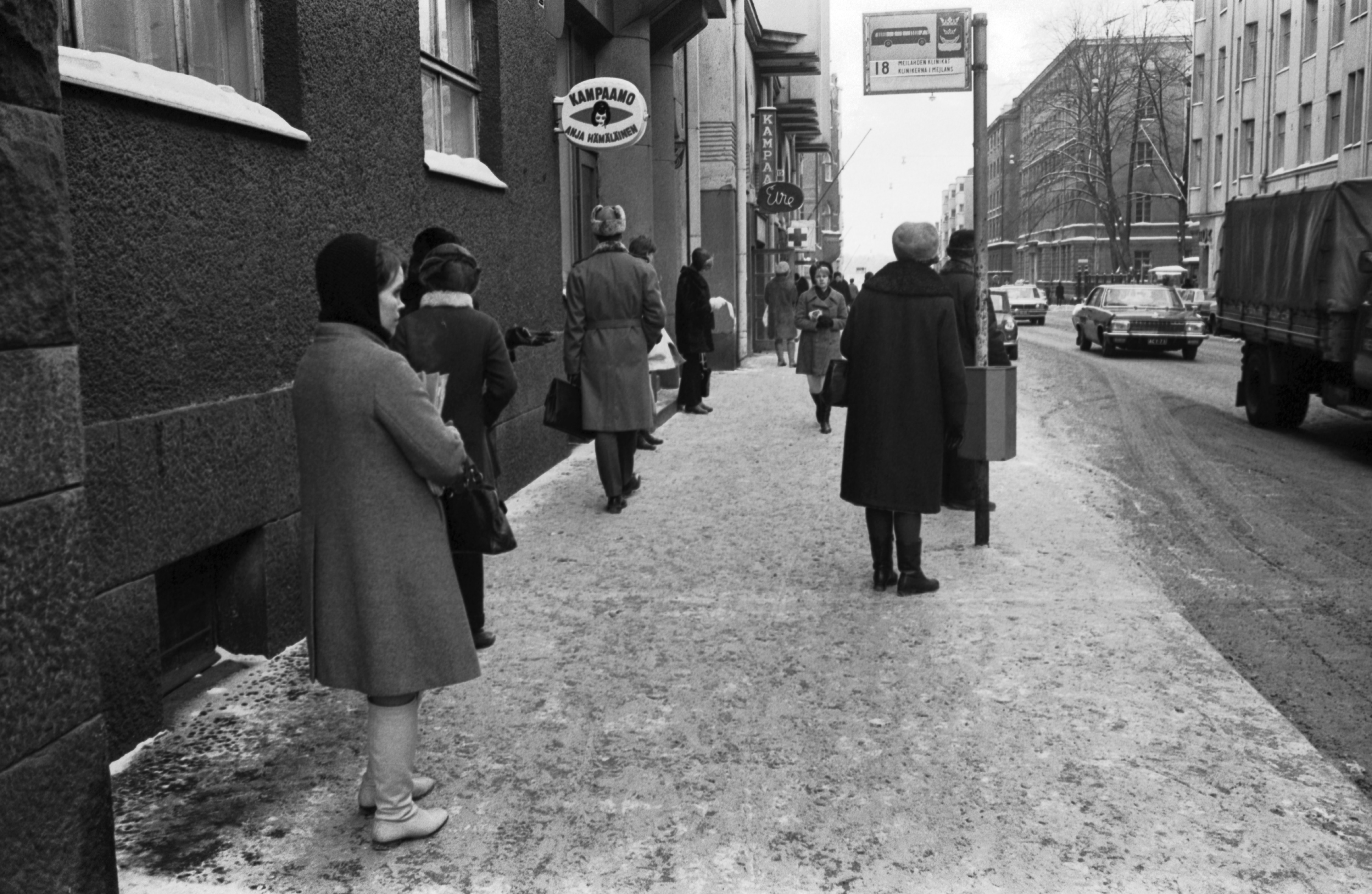 Ihmisiä bussi numero 18:n pysäkillä Liisankadulla. Talvi, lunta maassa. Taustalla näkyy Kampaamo Anja Hämäläisen kyltti.