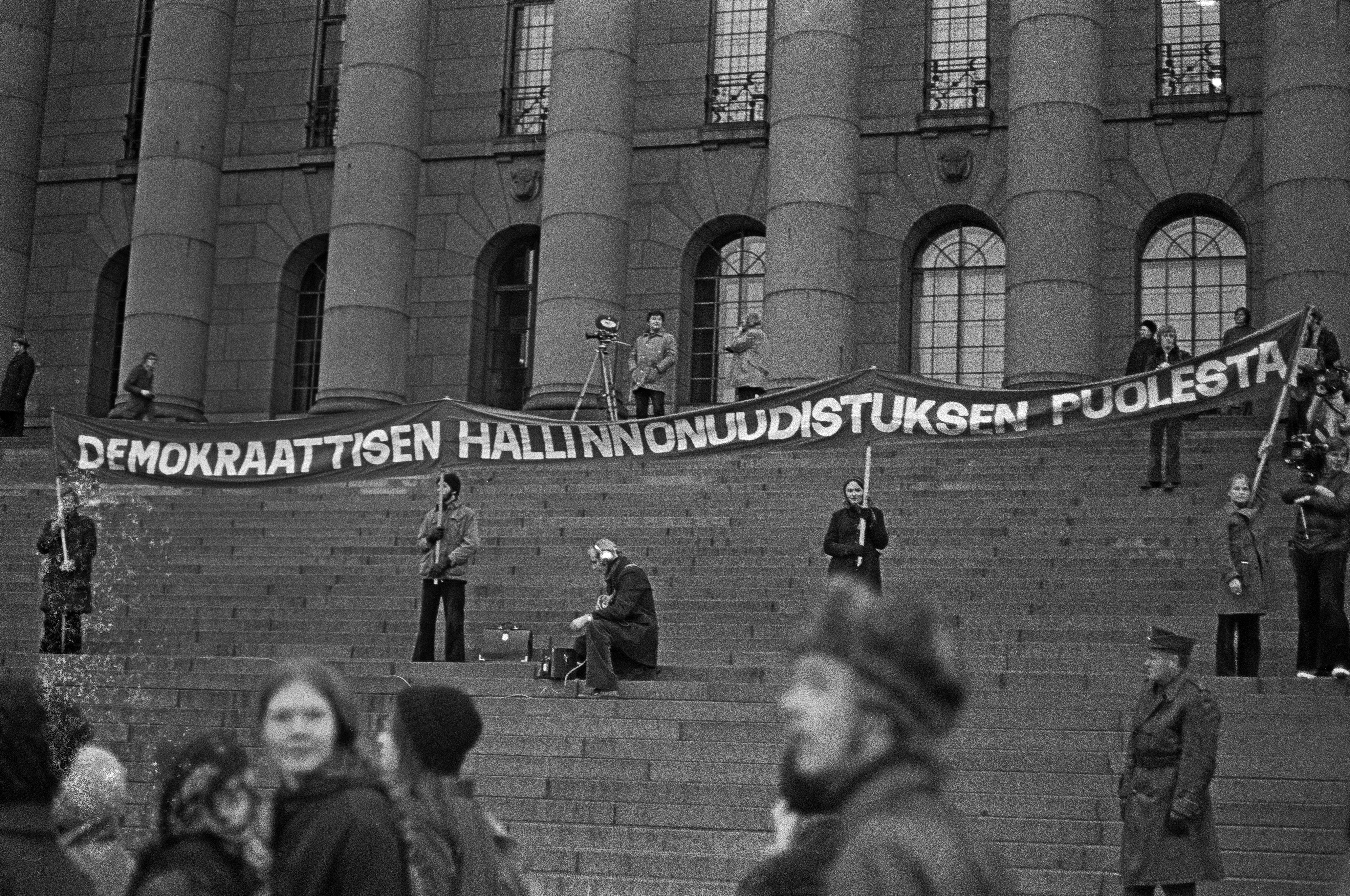 Mielenosoitus, jolla opiskelijaliike vaati yleistä ja yhtäläistä äänioikeutta (yyä) yliopistojen ja korkeakoulujen hallintoelinten valintaperusteeksi. Mielenosoittajat pitävät pystyssä banderollia Eduskuntatalon portailla.