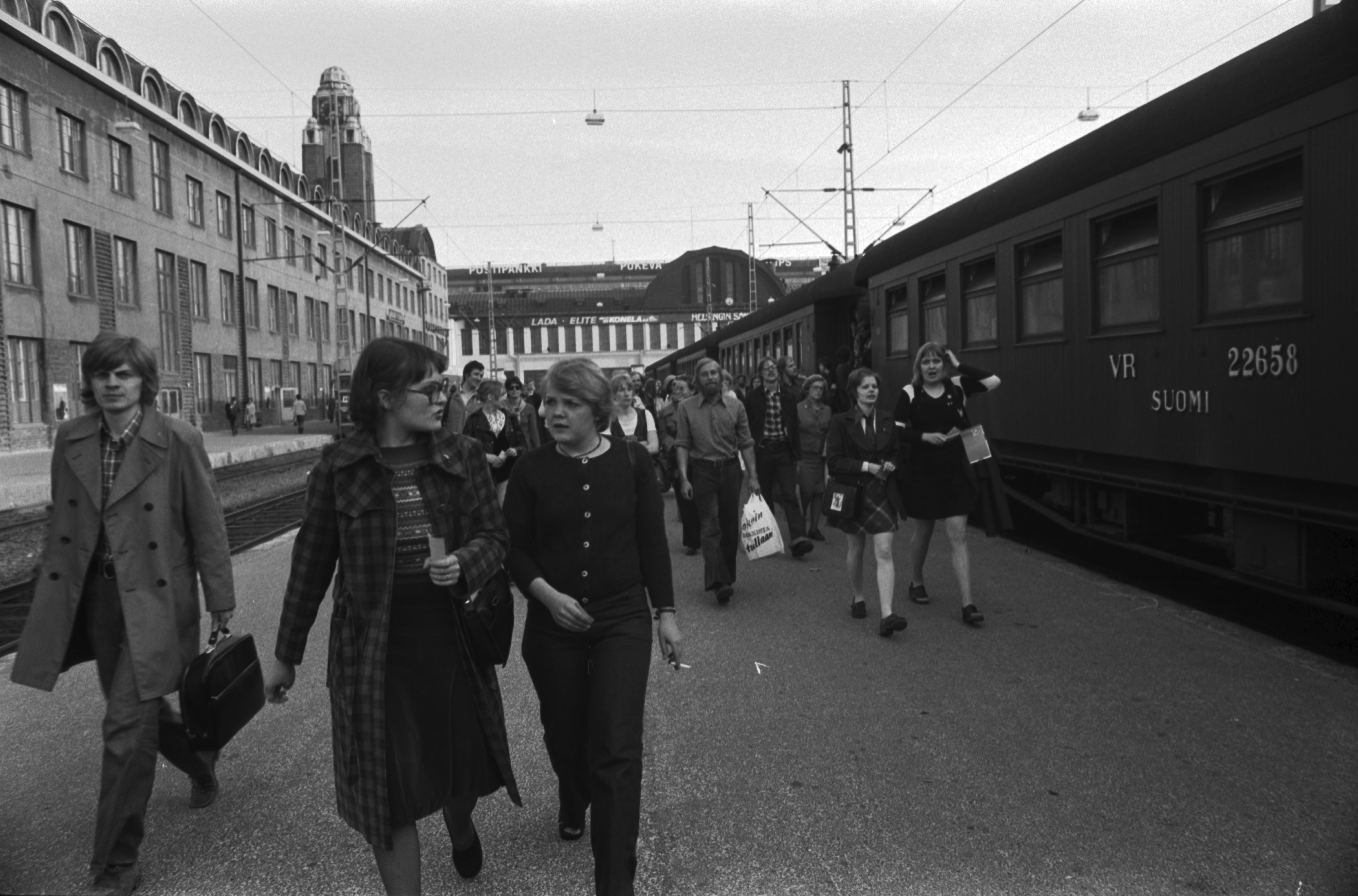 Helsingin rautatieasema. Ihmisiä Helsingin rautatieasemalla kiiruhtamassa sähköjunaan. Raiteilla oikealla VR:n puurunkoisia vaunuja.