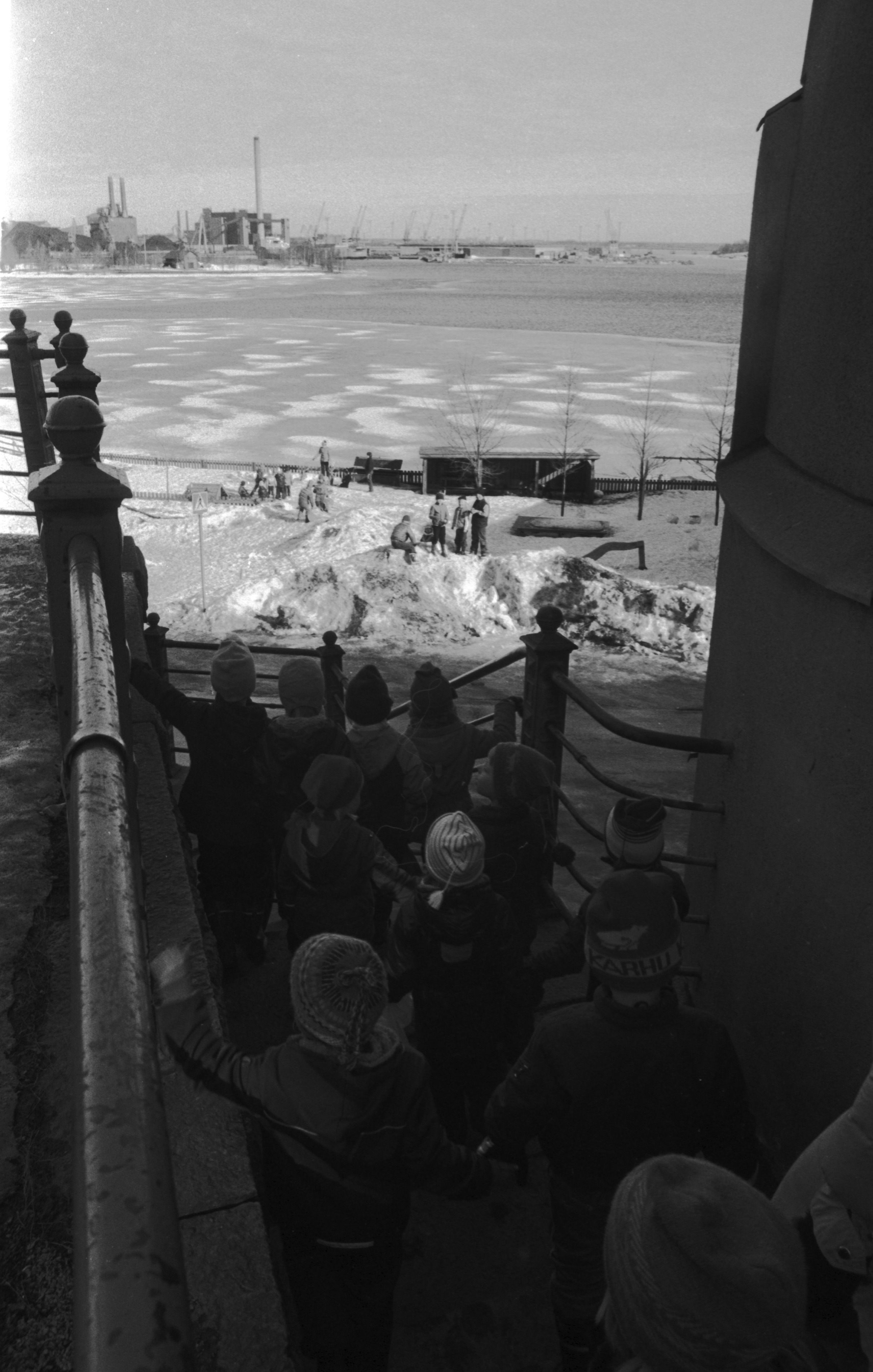 Laivastokatu. Vironniemen päiväkodin lapsia kulkemassa Vyökadulta alas Laivastokadulle johtavia portaita tutustumiskierroksella Katajanokkaan. Keskellä lapsia lumisessa Laivastopuistossa, taustalla Hanasaaren voimalat.