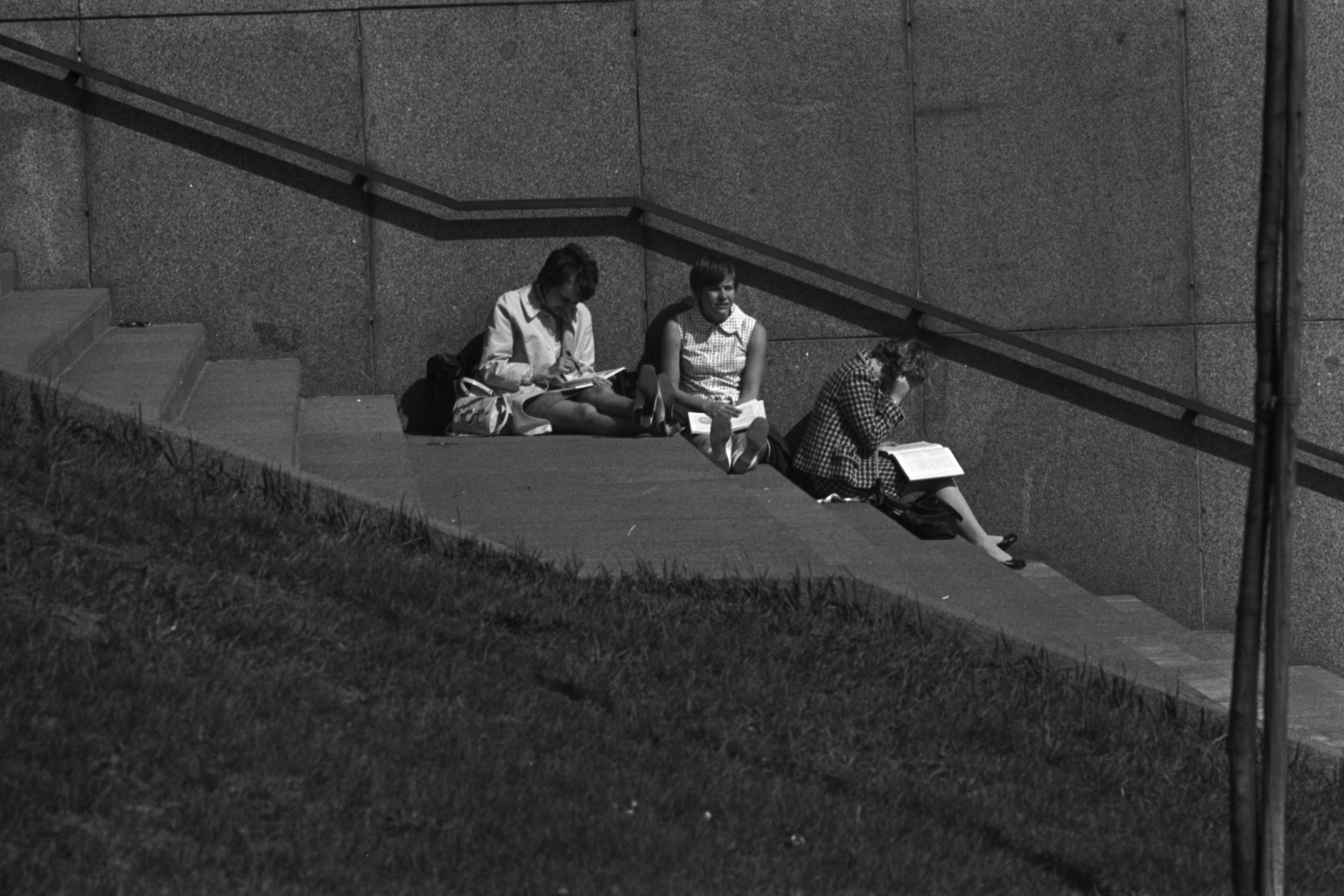 Eläintarhantie 3. Naisia lukemassa kevätauringossa Kallion virastotalon kupeessa olevilla portailla.