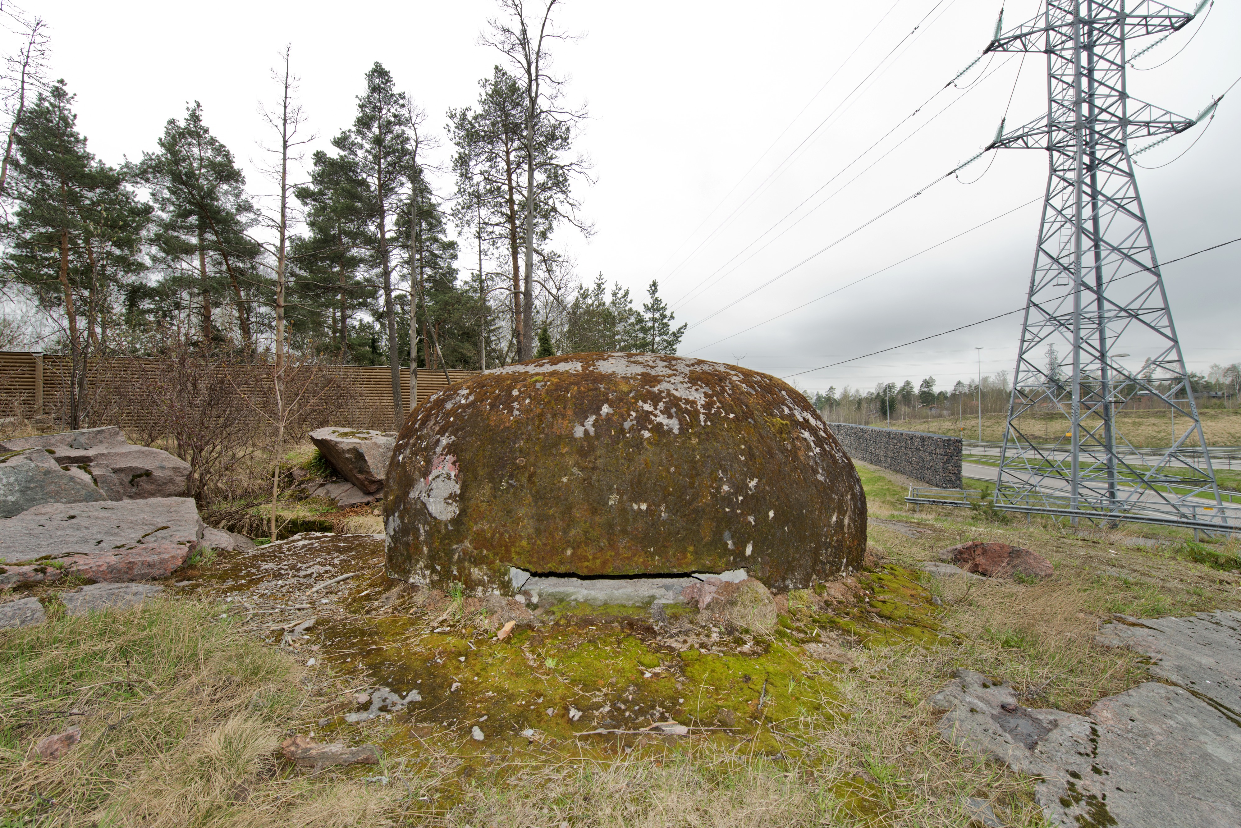 Ruukinranta. Ensimmäisen maailmansodan aikainen maalinnoitus, puolustusasema XXXVI:2 Ruukinrannassa, Espoossa. Kuvassa on linnoitteen länsipäässä sijaitseva pyöreä, kupukattoinen kivääri- tai tähystysasema. Betonisen rakenteen päällyskupu siirrettiin 1970- luvulla tietöiden yhteydessä puolustusasemasta XXXVI:1 tälle paikalle, jossa oli samanlaisen, keskeneräiseksi jääneen aseman alaosa valmiina. Etualalla aseman seinässä näkyy tähystys- tai ampuma-aukko. Taustalla vasemmalla on puinen ja oikealla kivistä tehty meluvalli. Kivisen meluvallin edessä seisoo voimajohtopylväs. Kuvaussuuntana lounas.