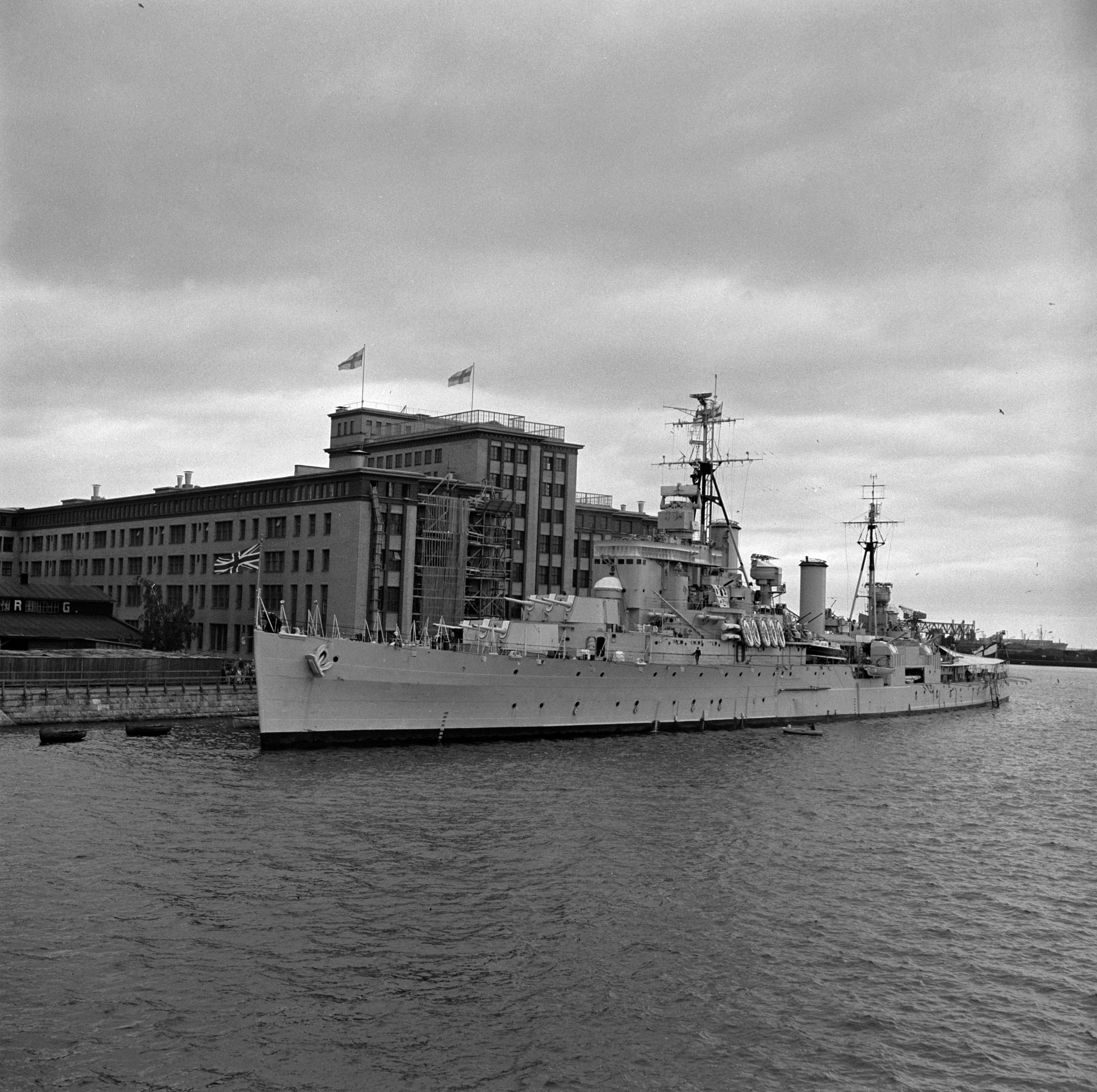HMS Swiftsure, Ison Britannian Royal Navy -alus, joka saattoi prinssi Philipiä tämän matkalla Helsingin olympialaisiin. Alus on ankkurissa Kaapelitehtaan edustalla.  (Alus oli toiminut sota-aluksena Kaukoidässä toisessa maailmansodassa.) Edessä Lauttasaarensalmi.  Kaapelitehdas, Tallberginkatu 1.