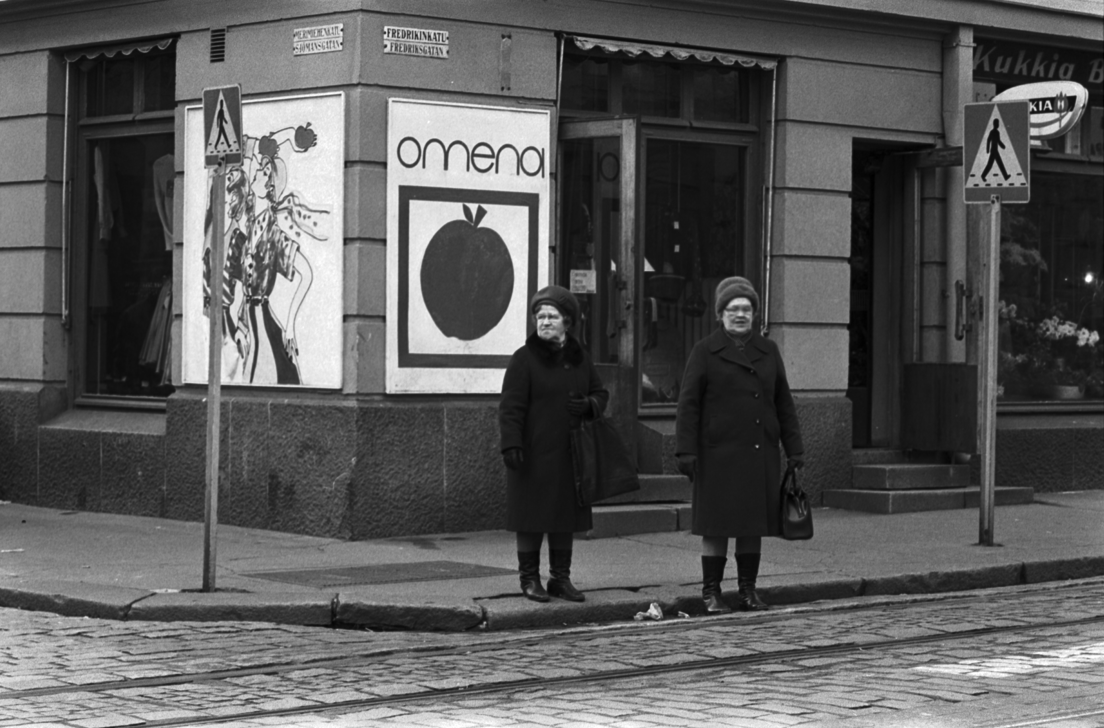 Fredrikinkatu 16. Kaksi naista asusteliike Omenan edessä Fredrikinkadun ja Merimiehenkadun kulmassa aikeissa ylittää kadun.