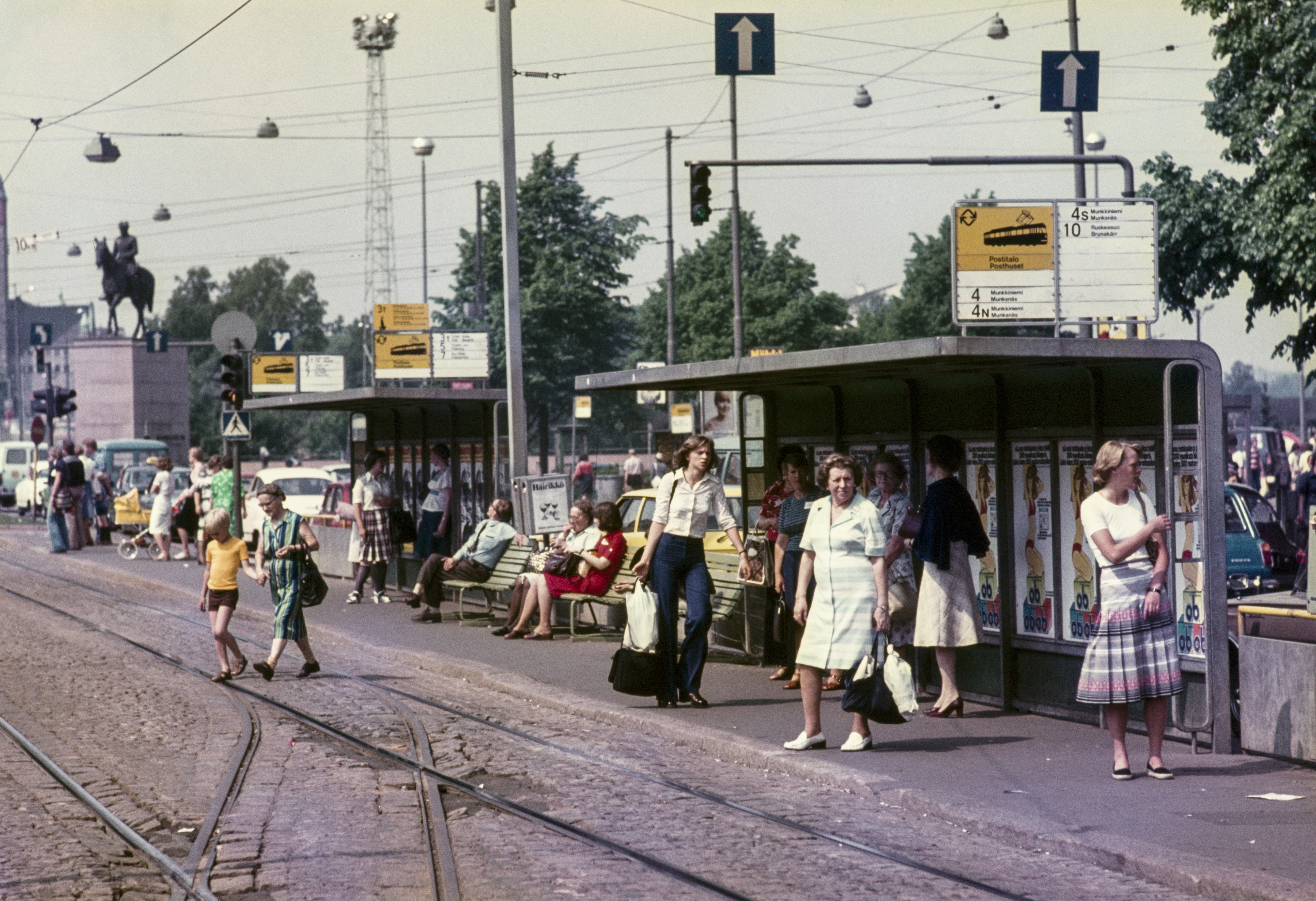 Ihmisiä raitiovaunupysäkillä Mannerheimintiellä tavaratalo Sokoksen kohdalla. Vasemmassa reunassa Mannerheimin ratsastajapatsas.