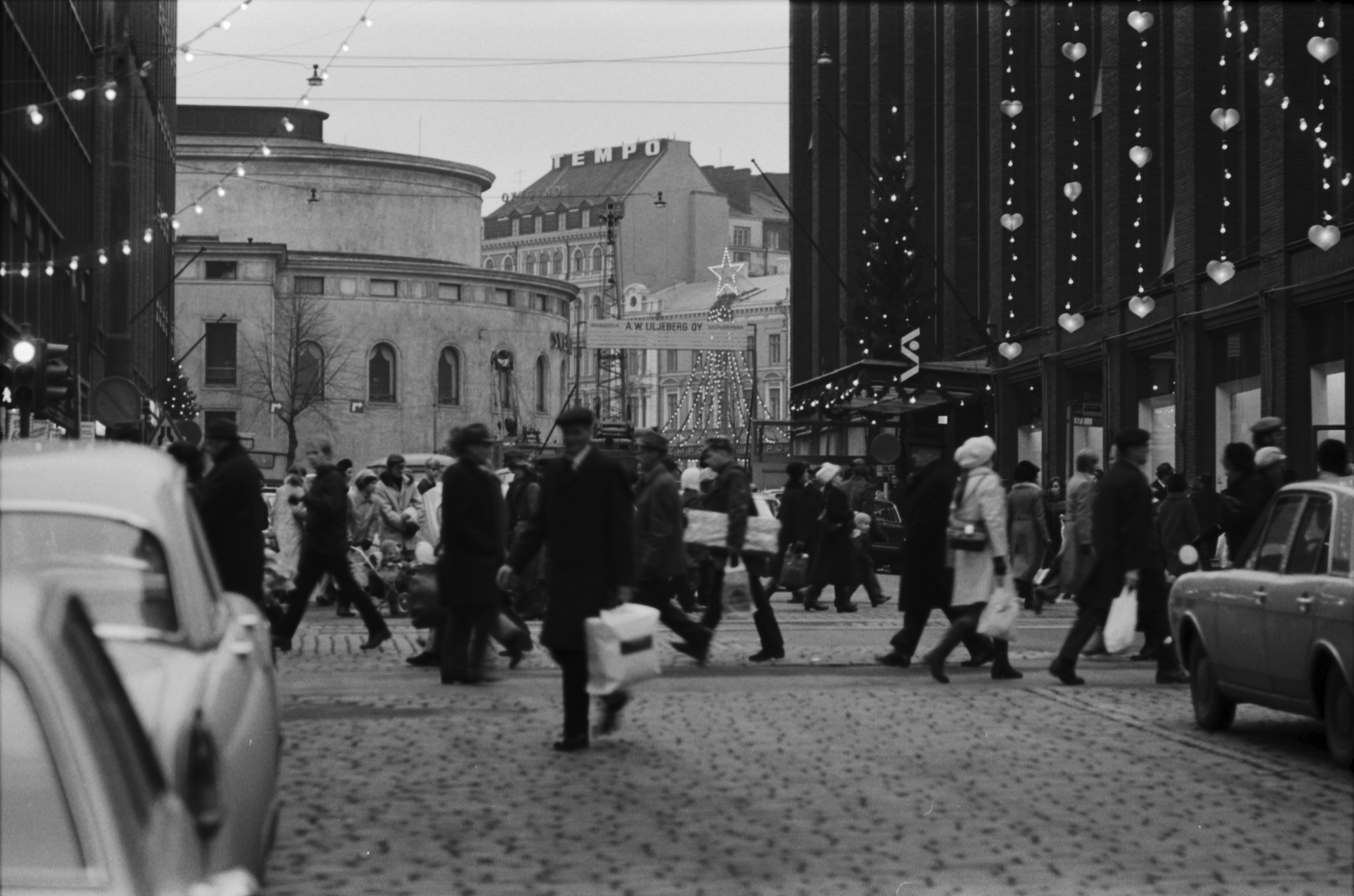 Keskuskatu 2. Jouluostoksilla olevia ihmisiä Aleksanterinkadulla Keskuskadun kulmassa. Oikealla Stockmannin tavaratalo, vasemmalla Ruotsalainen teatteri. Näkymä etelään Mannerheimintien suuntaan, jossa joulukoristeltu Tempon tavaratalo.
