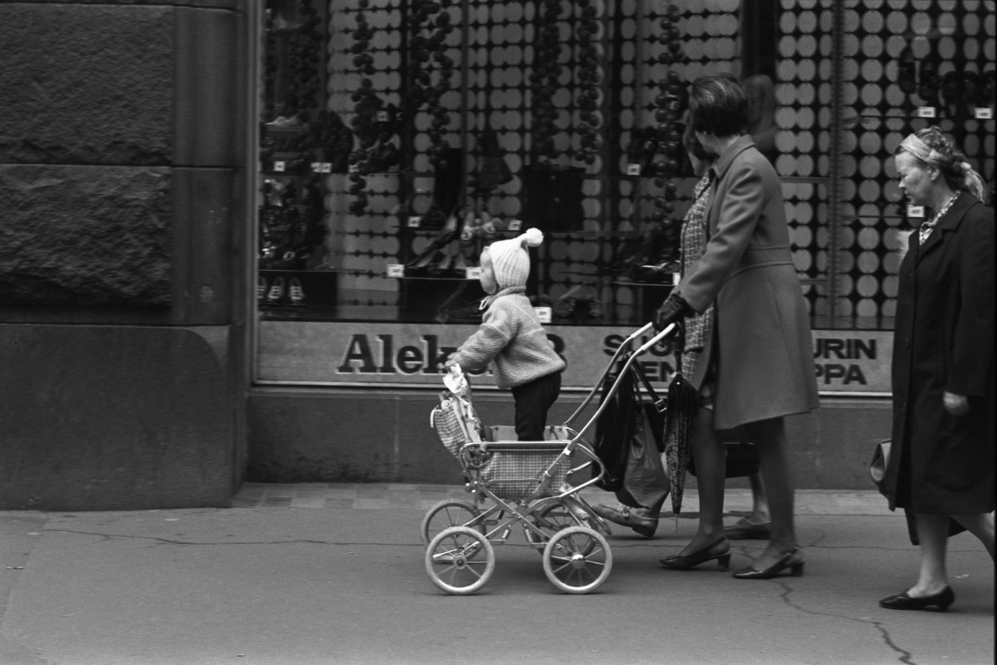 Aleksanterinkatu 13. Rattaissa seisovaa lasta työtävä nainen Aleksanterinkadulla kävelykatukokeilun aikaan.