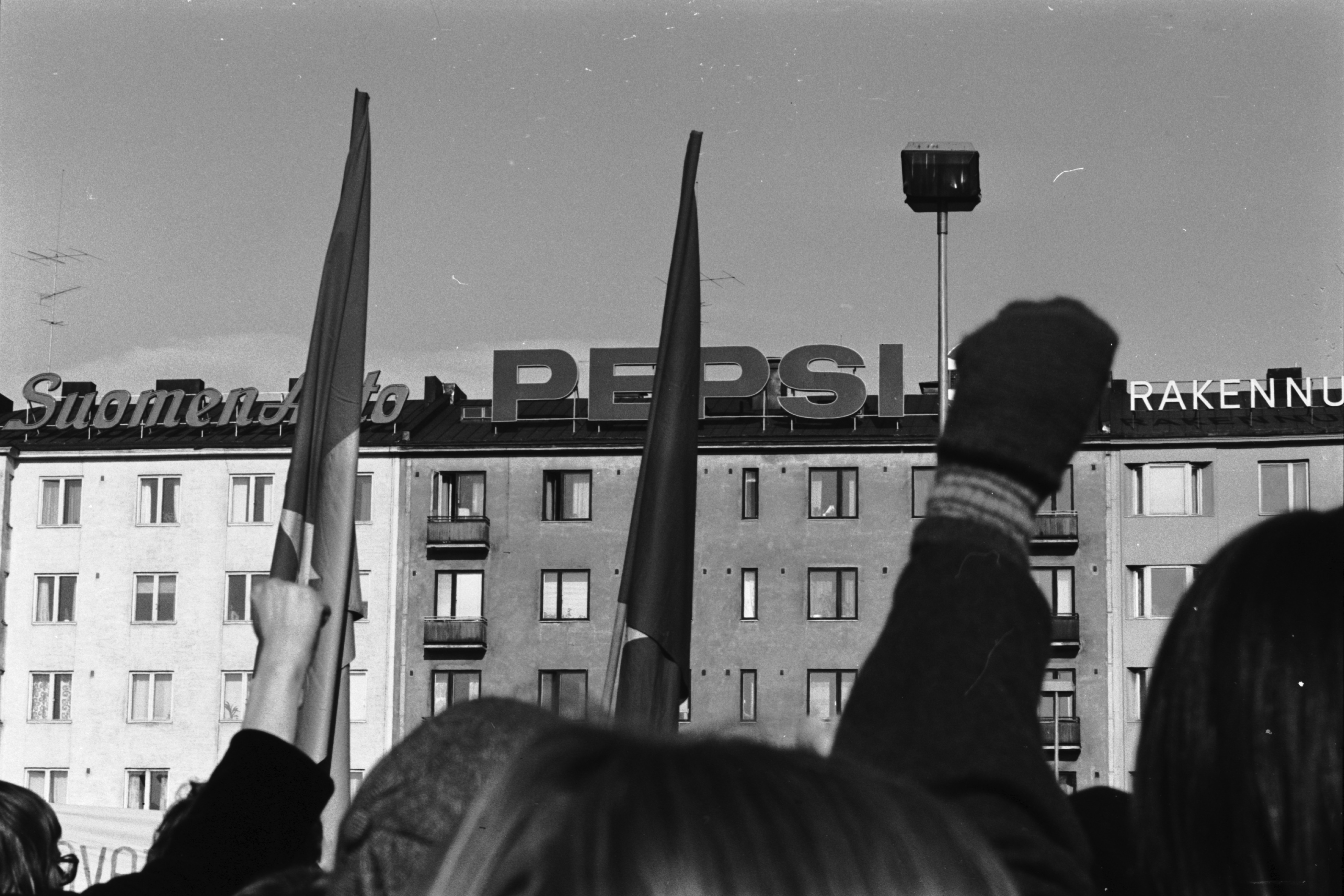 Vietnamin sodan vastaiseen mielenosoitukseen osallistuvia ihmisiä nyrkit pystyssä marssin päätepisteessä Hakaniementorilla. Taustalla Viherniemenkatu 7:n talon katolla Pepsi-mainoskirjaimet.