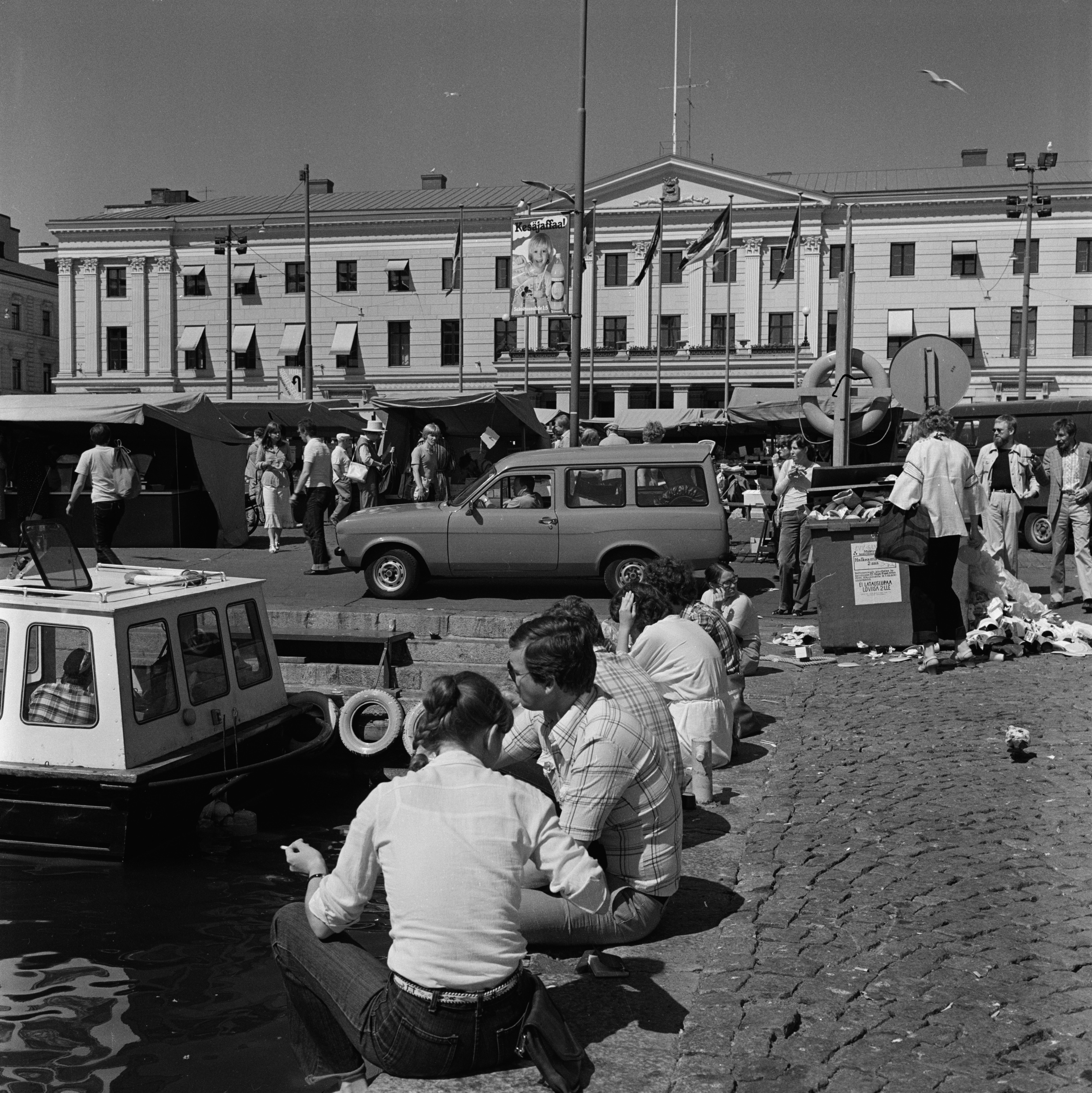 Kauppatori. Ihmisiä istumassa Kolera-altaan reunalla. Taustalla Kaupungintalo.