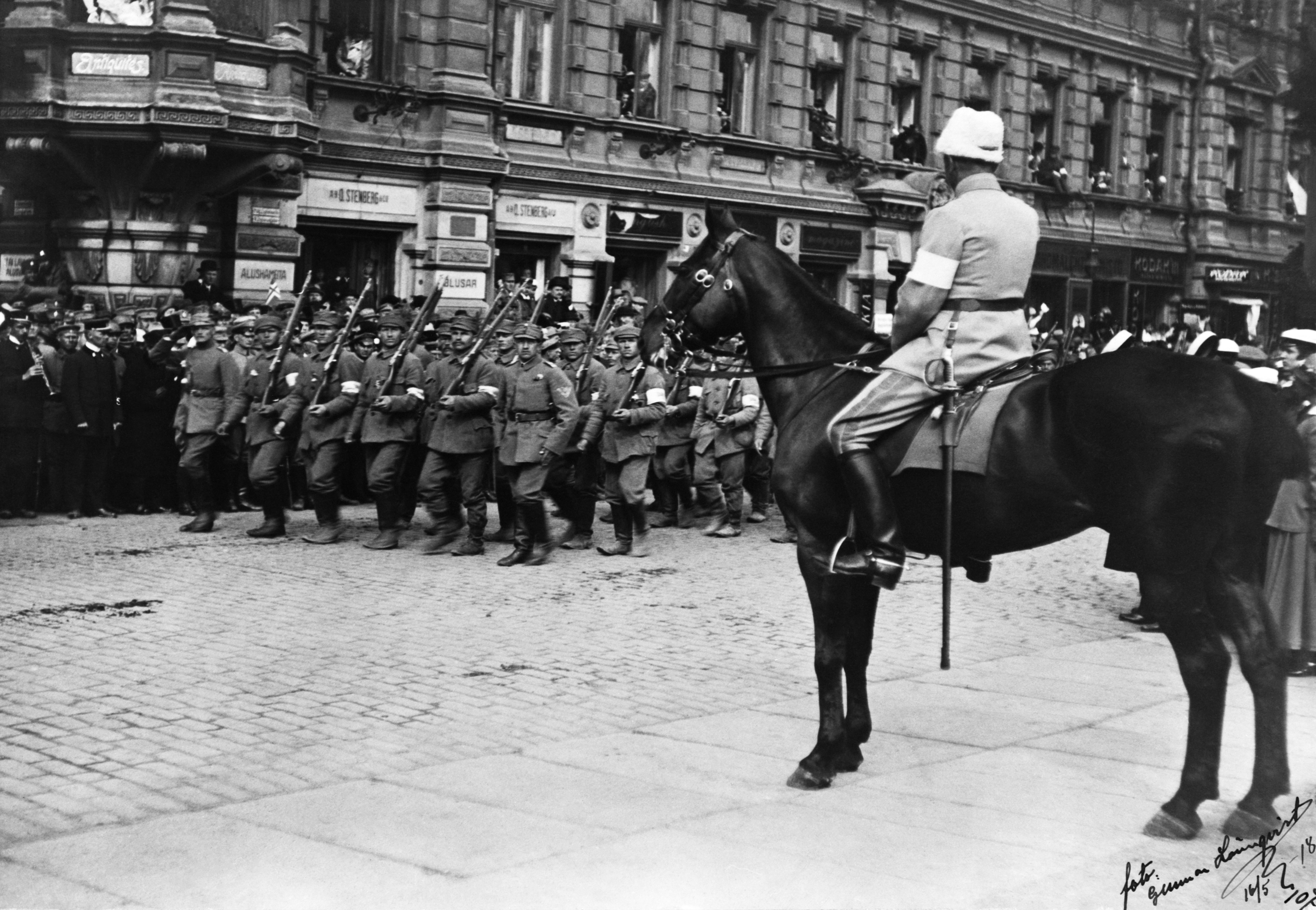 Helsingin valtaus, voitonparaati 16.5.1918. Valkoisen armeijan ylipäällikkö C.G.E. Mannerheim ottaa hevosen selässä istuen vastaan joukkojen ohimarssin. Taustalla ns. Grönqvistin talo, Pohjoisesplanadi 25-27.