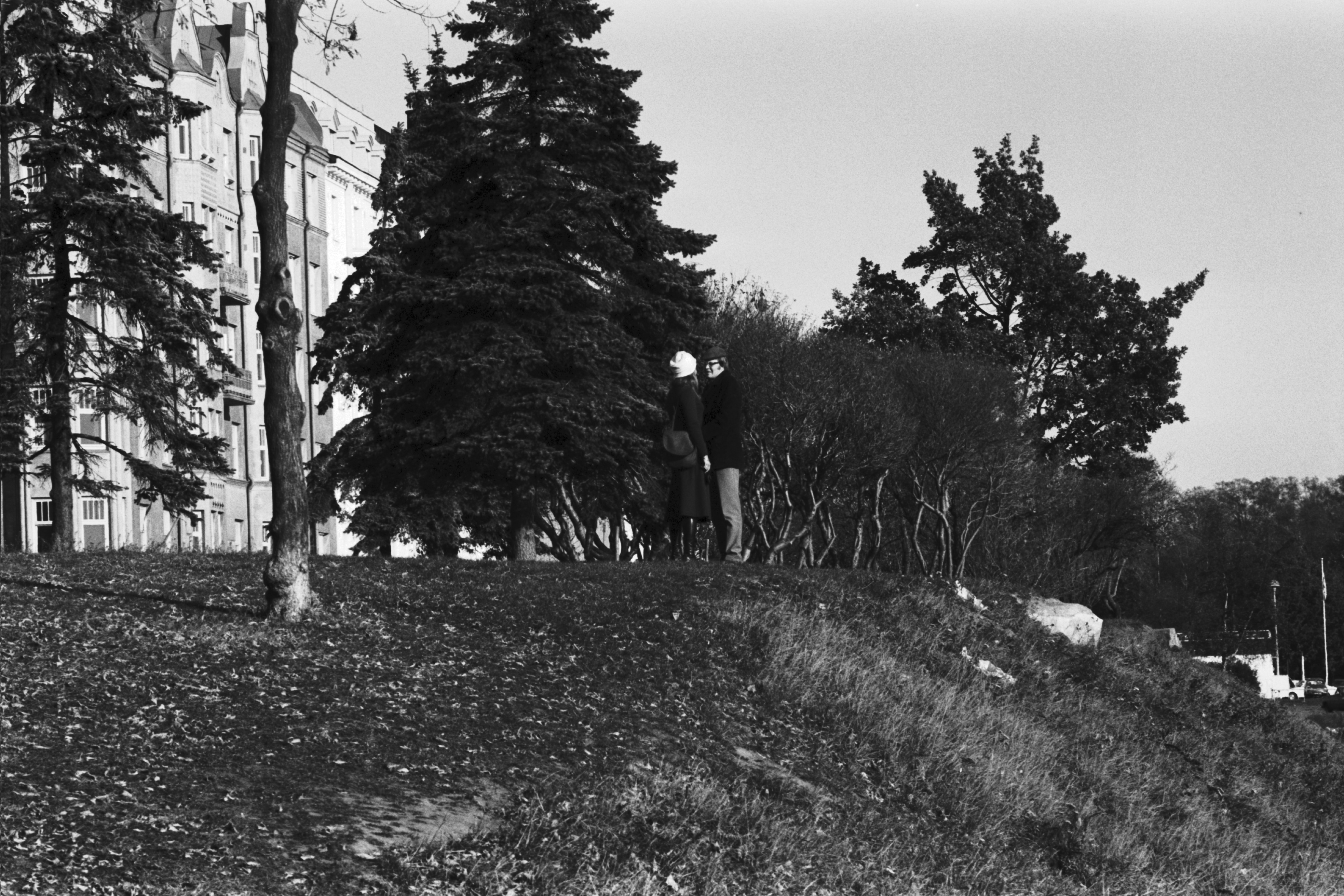 Ullanlinna. Nainen ja mies seisomassa Fredrik Stjernvallin puistossa. Taustalla vasemmalla häämöttää Merikatu 9:n kerrostalo.