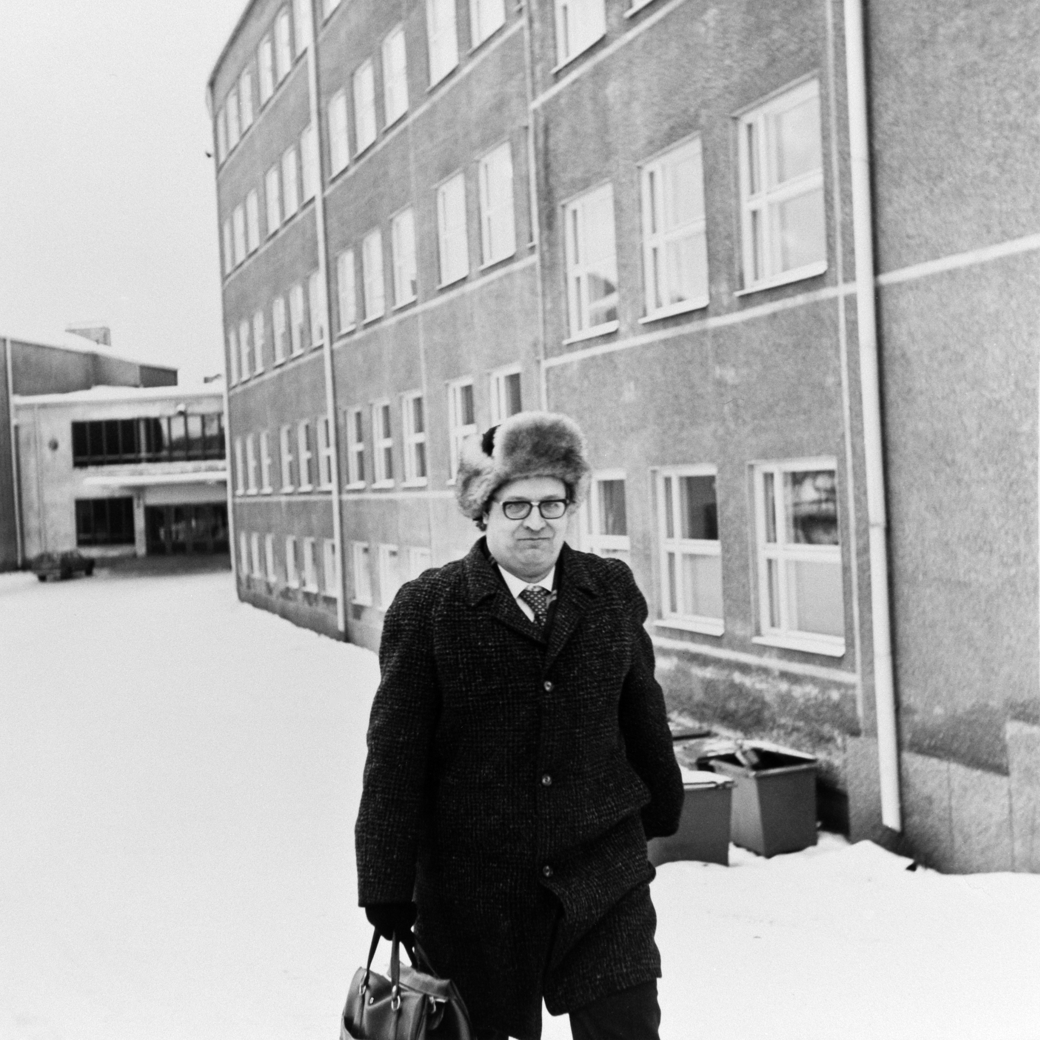 Suomen kielen opettaja seisoo Hykkylän koulun ja lukion (ent. Helsingin kaksoisyhteislyseo, nyk. Helsingin luonnontiedelukio) lumisella pihalla, Mäkelänkatu 93. Vuonna 1955 valmistuneessa rakennuksessa toimii nykyään Käpylän peruskoulu.