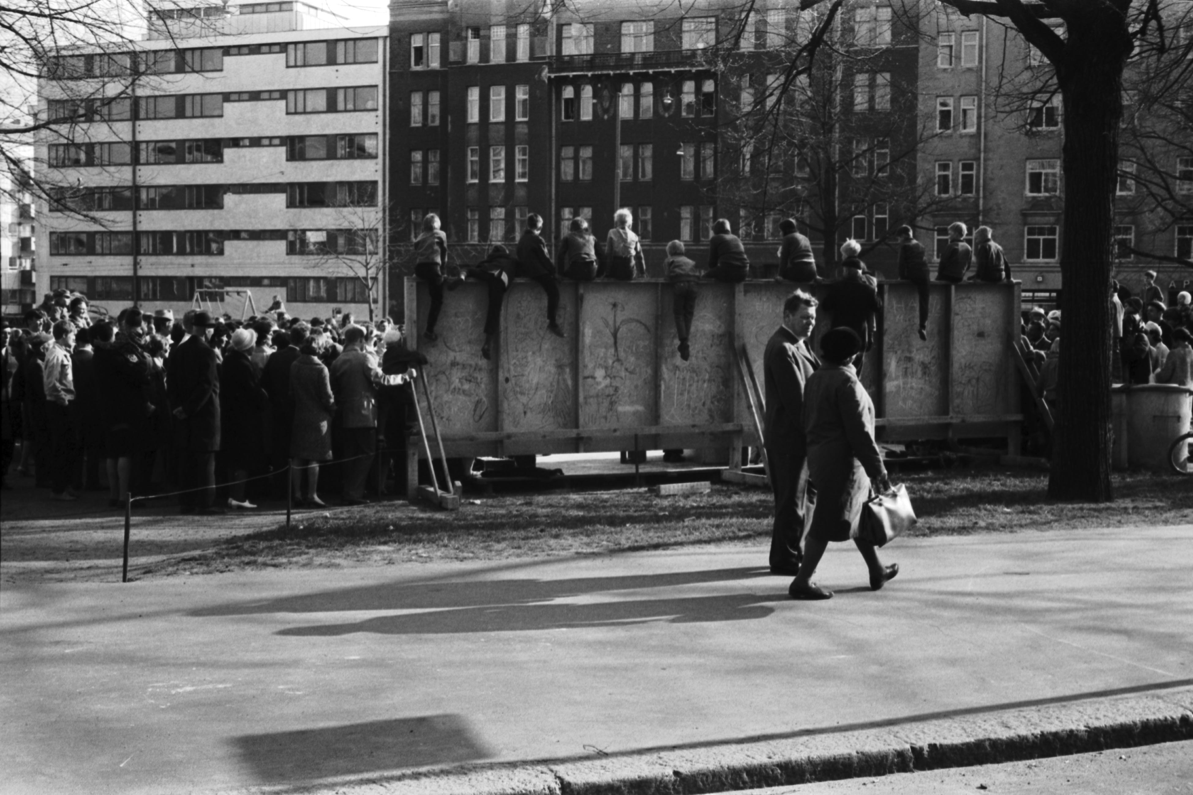 Karhupuisto. Helsingin juhlaviikot. Ihmisiä seuraamassa esitystä Karhupuistossa puistotapahtuman aikaan. Jotkut pojat ovat kiivenneet esiintymislavan takaseinän päälle. Näkymä Agricolankadun suunnalta.