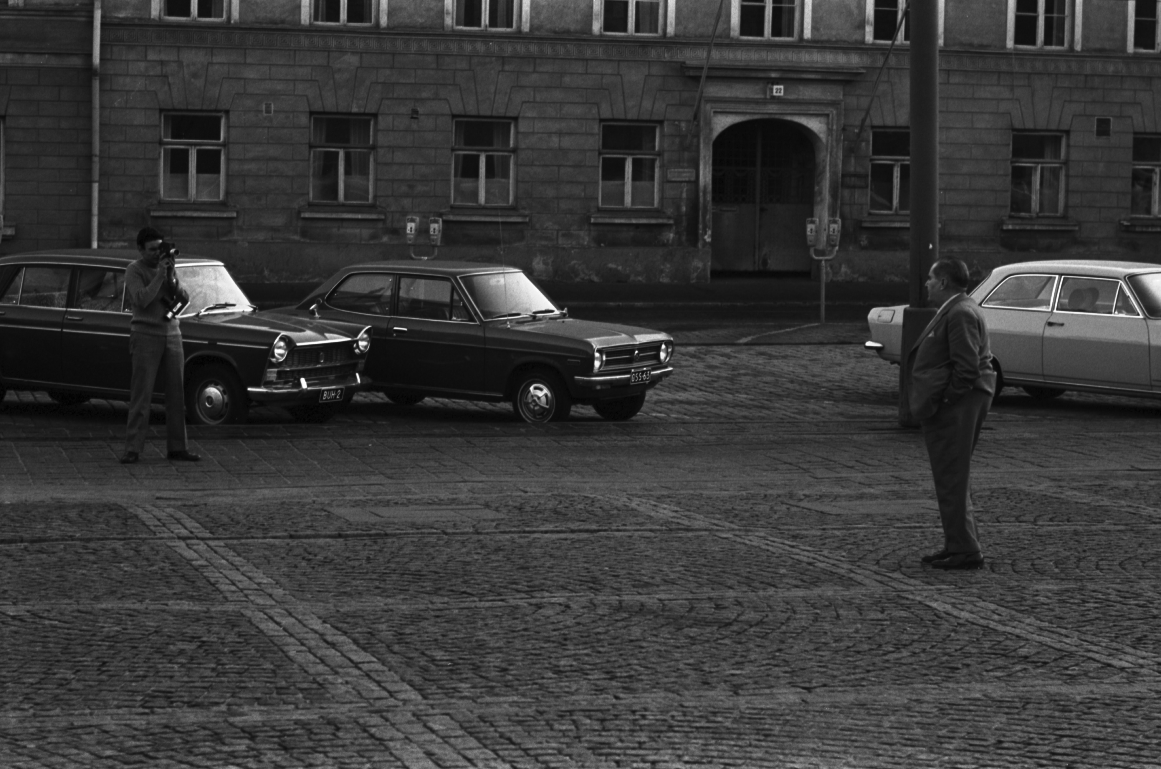 Kruununhaka, Senaatintori. Mies kaitafilmaamassa toista miestä Senaatintorilla Aleksanterinkatu 22:n kohdalla. Taustalla pysäköityjä autoja: Fiat 1800, Datsun 1200 "Finn" ja Opel Rekord.