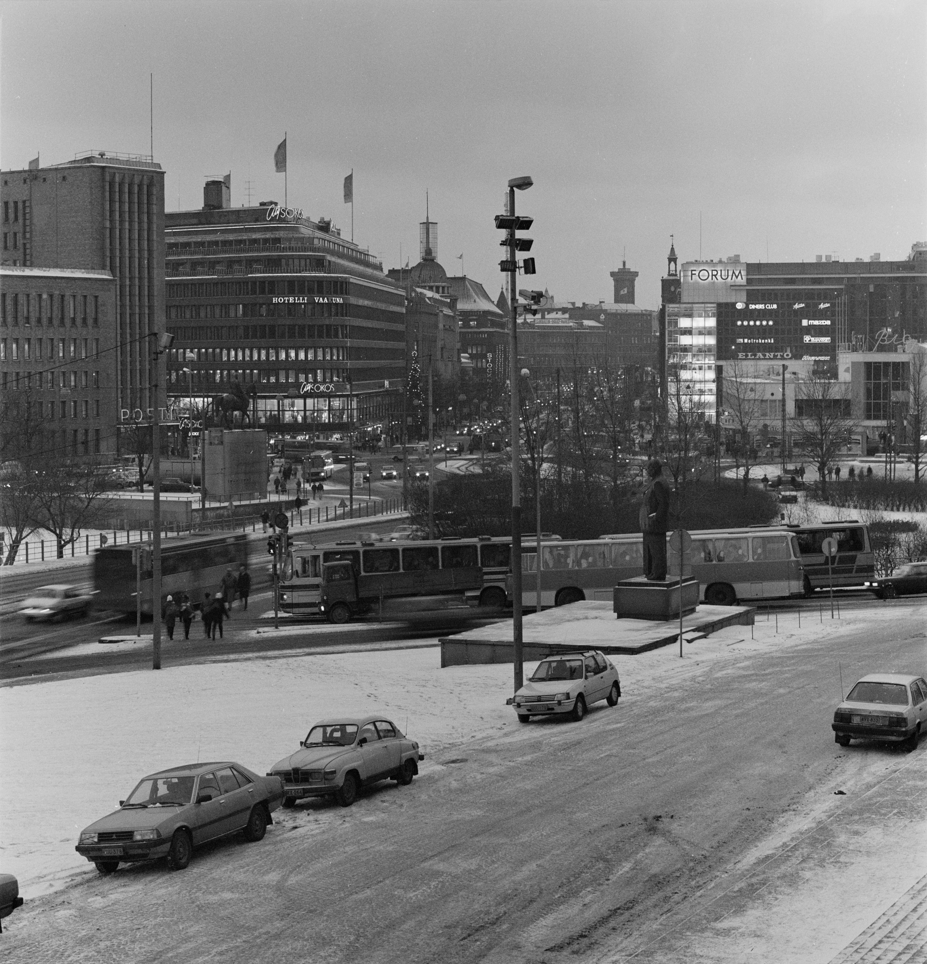 Liikennettä Mannerheimintiellä ja Pohjoisella Rautatiekadulla. Pysäköityjä autoja Eduskuntatalon edessä. Näkymä Eduskuntatalon portailta keskustaan päin.