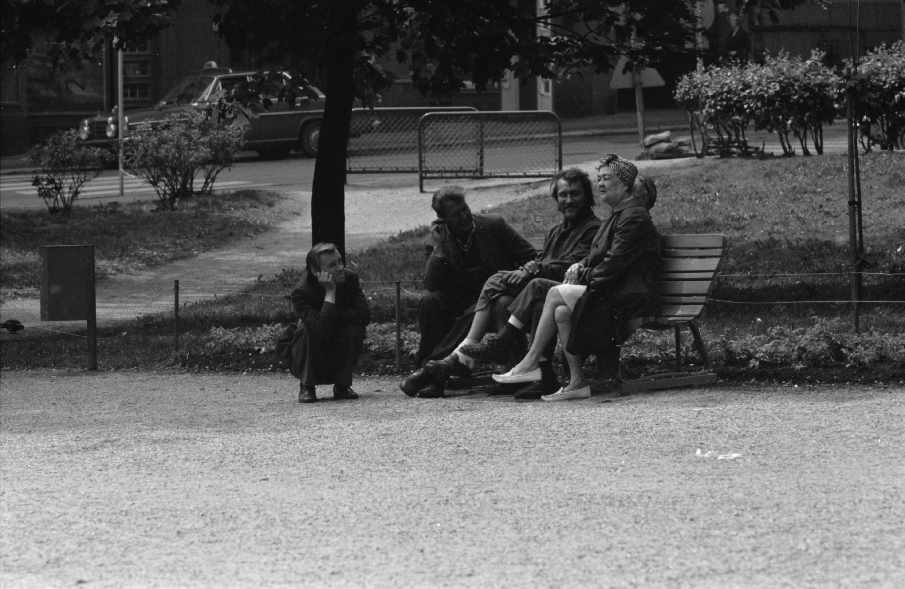 Liisanpuistikko. Ihmisiä, puistojen miehiä, yksi kyykyssä vieressä, ja nainen istumassa penkillä Liisanpuistikossa.