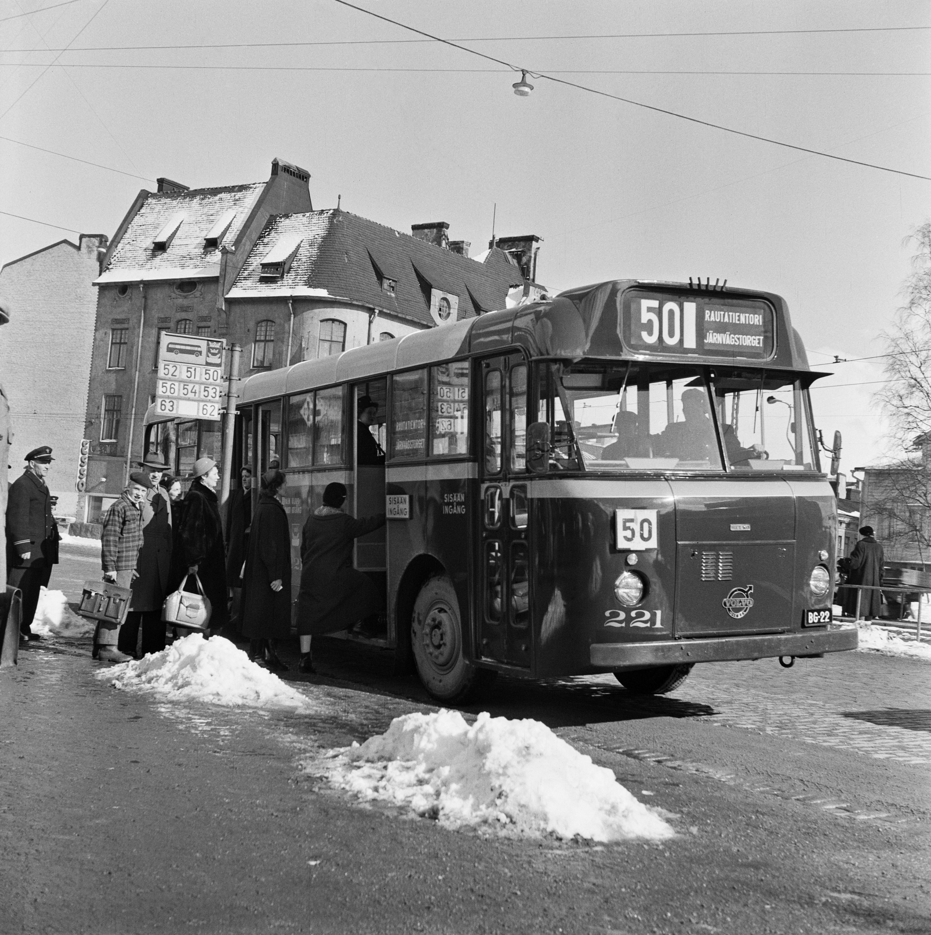Matkustajia nousemassa linja-autoon pysäkillä Hämeentien ja Helsinginkadun risteyksessä. Taustalla Hämeentie 33 - Vilhovuorenkatu 2.