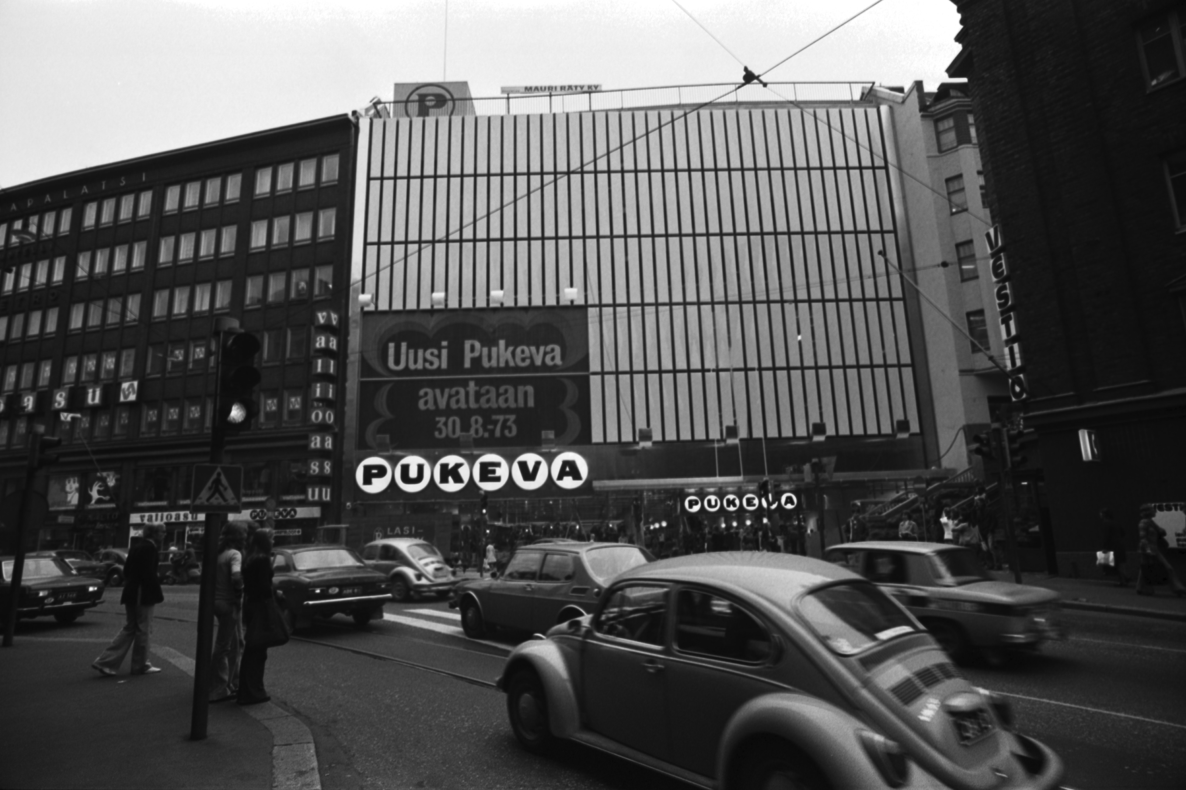 Kaisaniemenkatu 5. Pukevan uudistuneen tavaratalon julkisivua Kaisaniemenkadun suunnalta laajennusosan valmistuttua. Seinässä teksti: Uusi Pukeva avataan 30.8.1973.