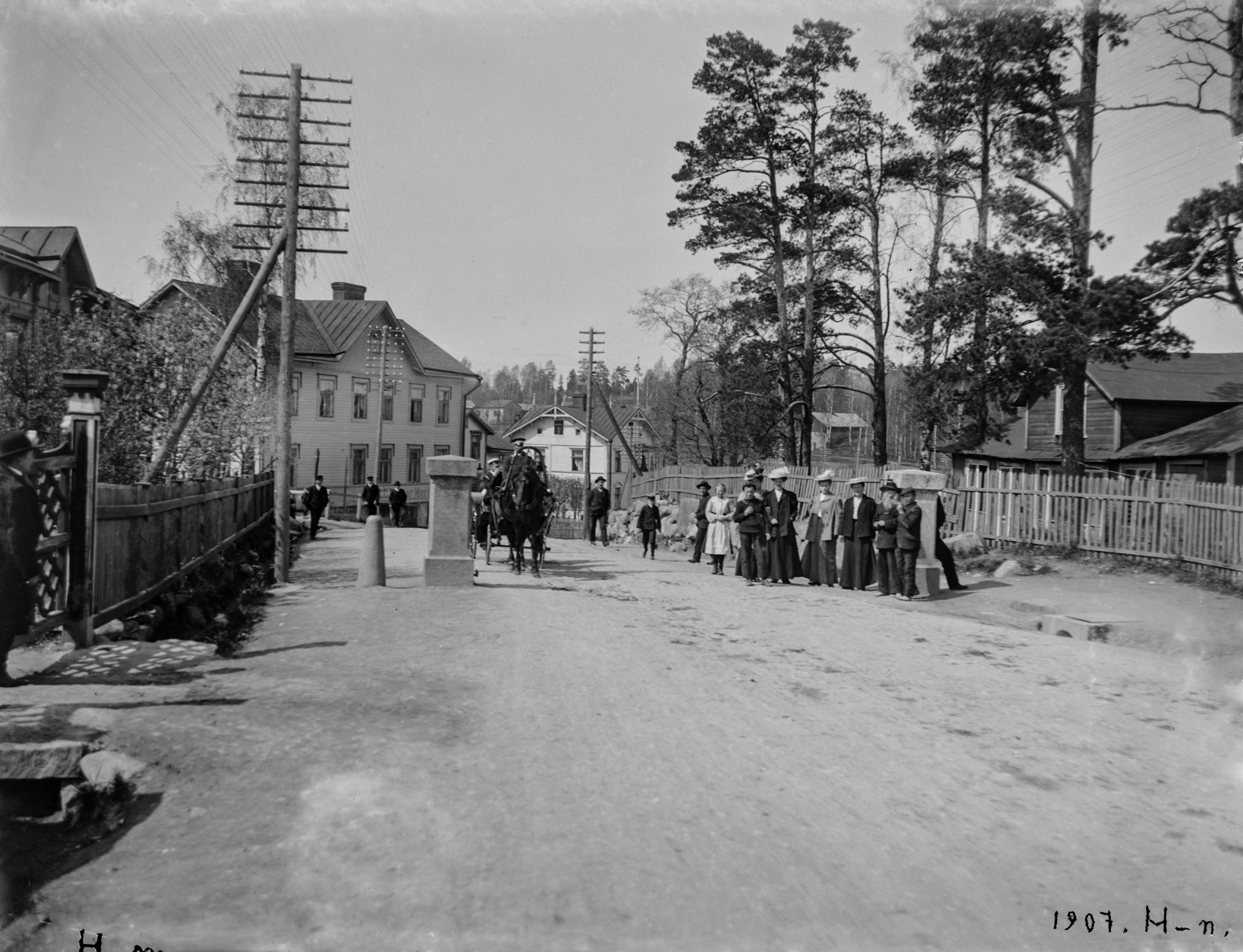 Väkeä kaupungin tulliportilla Itäisellä Viertotiellä (nykyinen Hämeentie). Oikealla Hermanni 41, Edward Forsbäckin talo ja pyrotekninen laboratorio.