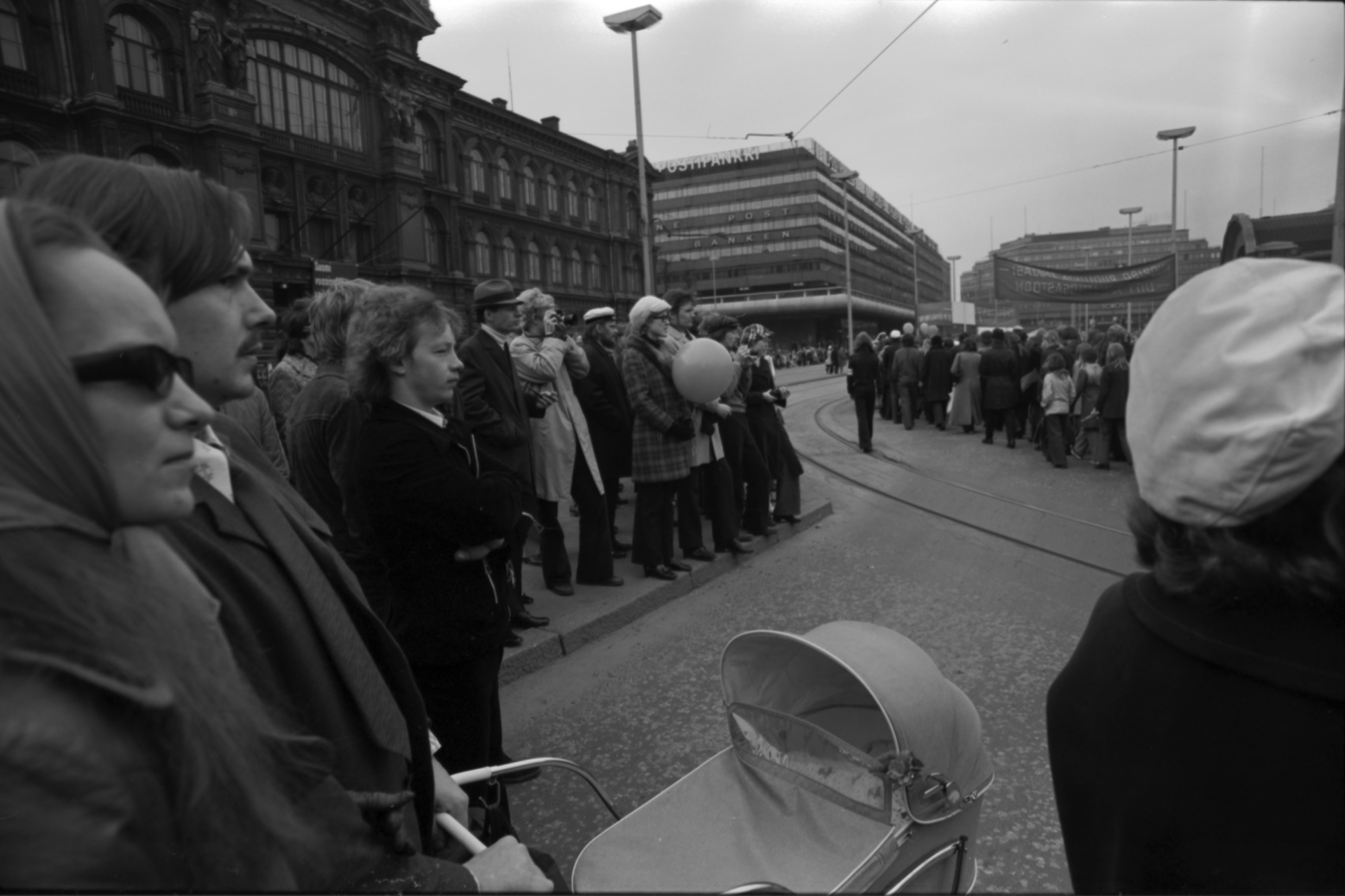 Kaivokatu. Yleisöä seuraamassa työväen vappukulkuetta Kaivokadun ja Mikonkadun kulmassa 1.5.1972. Näkymä Mikonkadun suunnalta Keskuskadulle päin. Etualalla lastenvaunut, vasemmalla Ateneumin rakennus.