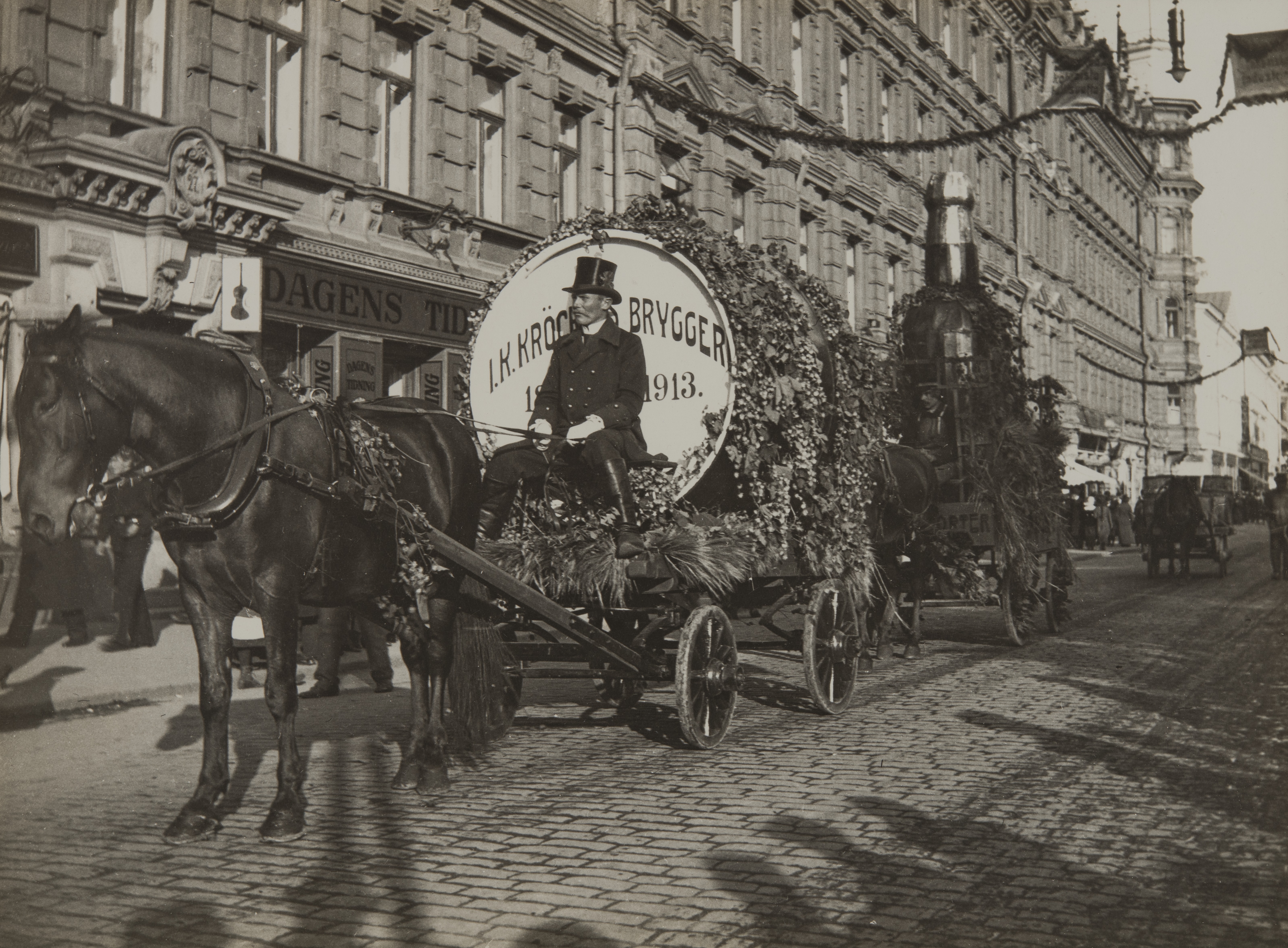 Juhlakulkue Pohjois Esplanaadikadulla (nyk. Pohjoisesplanadi) suomalaisen viikon (27.9.-4.10) aikaan vuonna 1913. Kulkueessa kaksi Pitäjänmäellä 1872 - 1921 toimineen J.K Kröckellsin panimoa mainostanutta hevosten vetämää kärryä, joista etummaisessa iso oluttynnyri ja taaemmassa iso portteripullo. Taustalla ns. Grönqvistin talo, Pohjoisesplanadi 25-27.