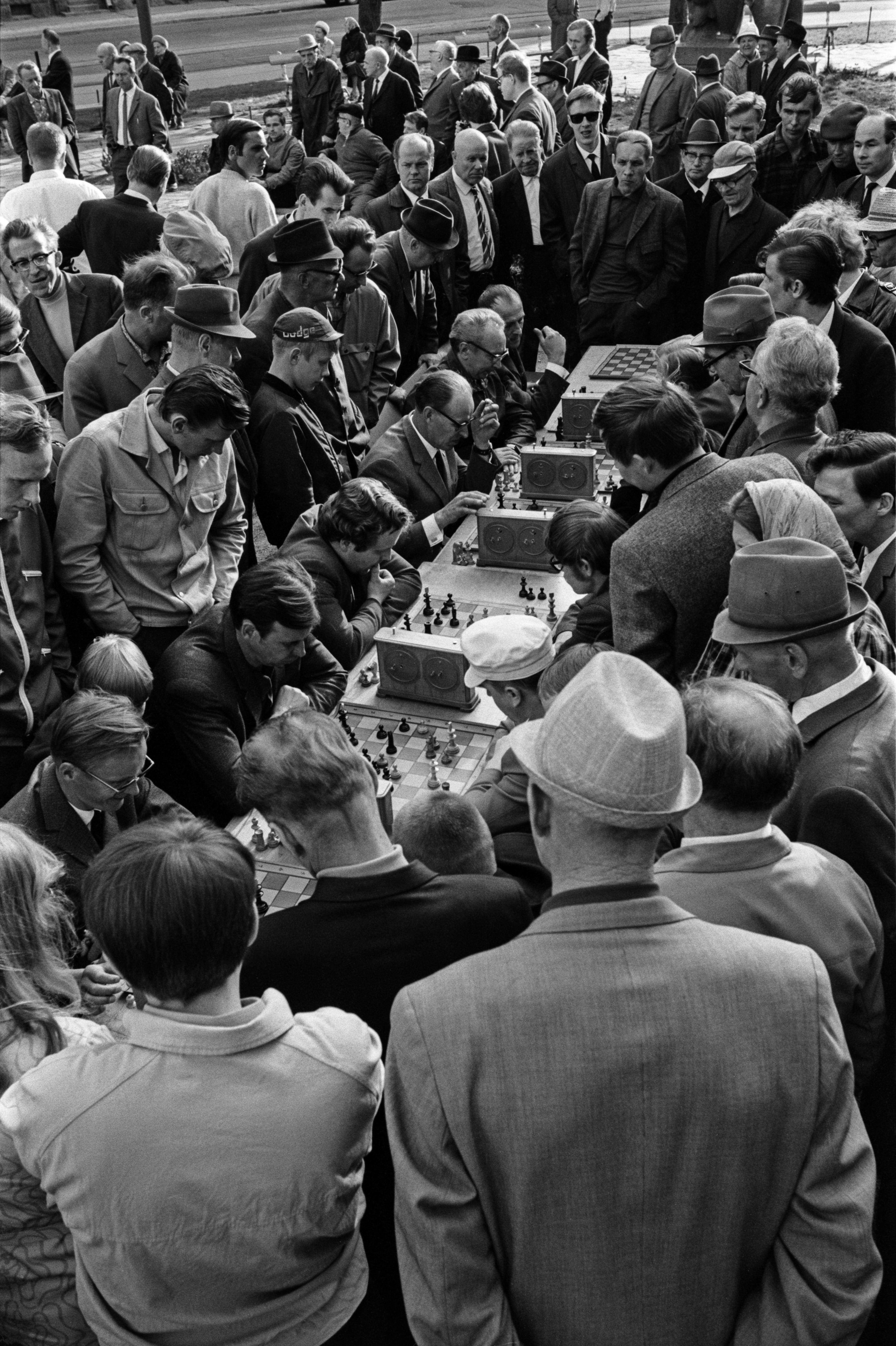 Karhupuisto. Helsingin juhlaviikot. Miehiä pelaamassa shakkia pitkän pöydän ääressä sankan yleisön seuratessa tapahtumaa Karhupuistossa puistotapahtuman aikaan.