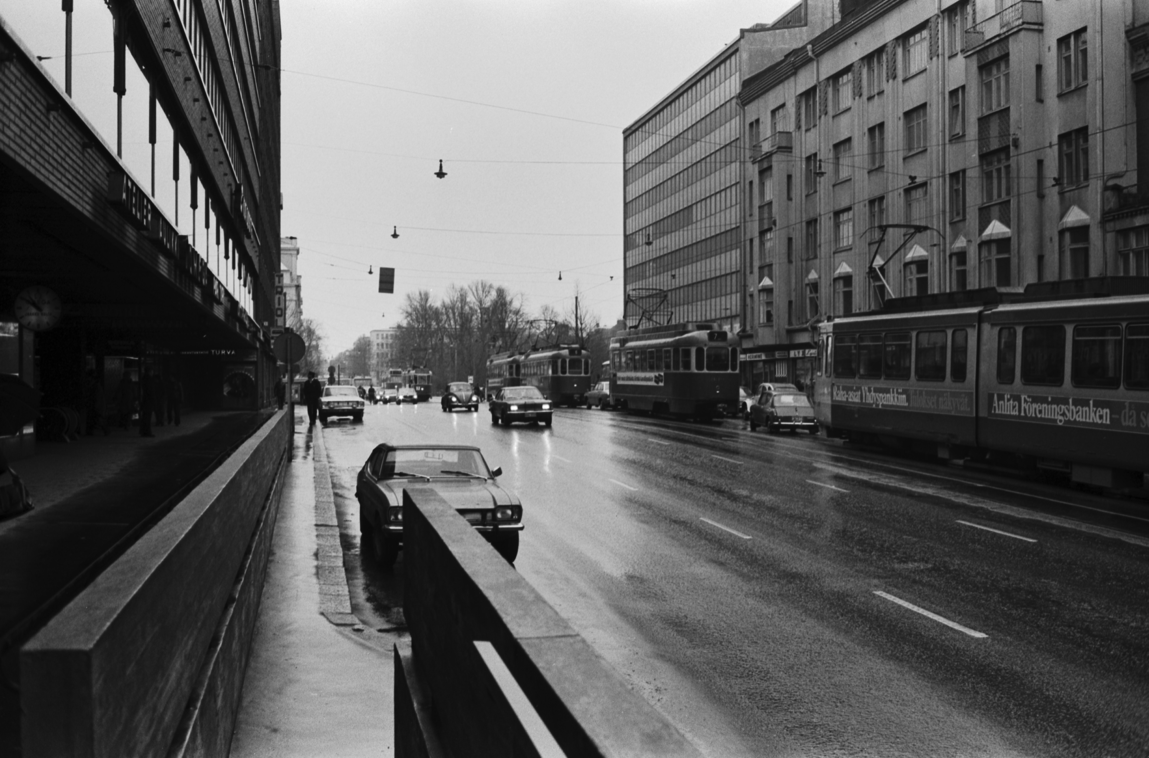 Siltasaarenkatu. Näkymä sateiselta Siltasaarenkadulta Hakaniemenrannan kulmalta Pitkänsillan suuntaan. Pysäköidyt autot edestä taakse: Ford Capri, Dodge Dart. Liikenteessä: Ford Taunus, Volkswagen.