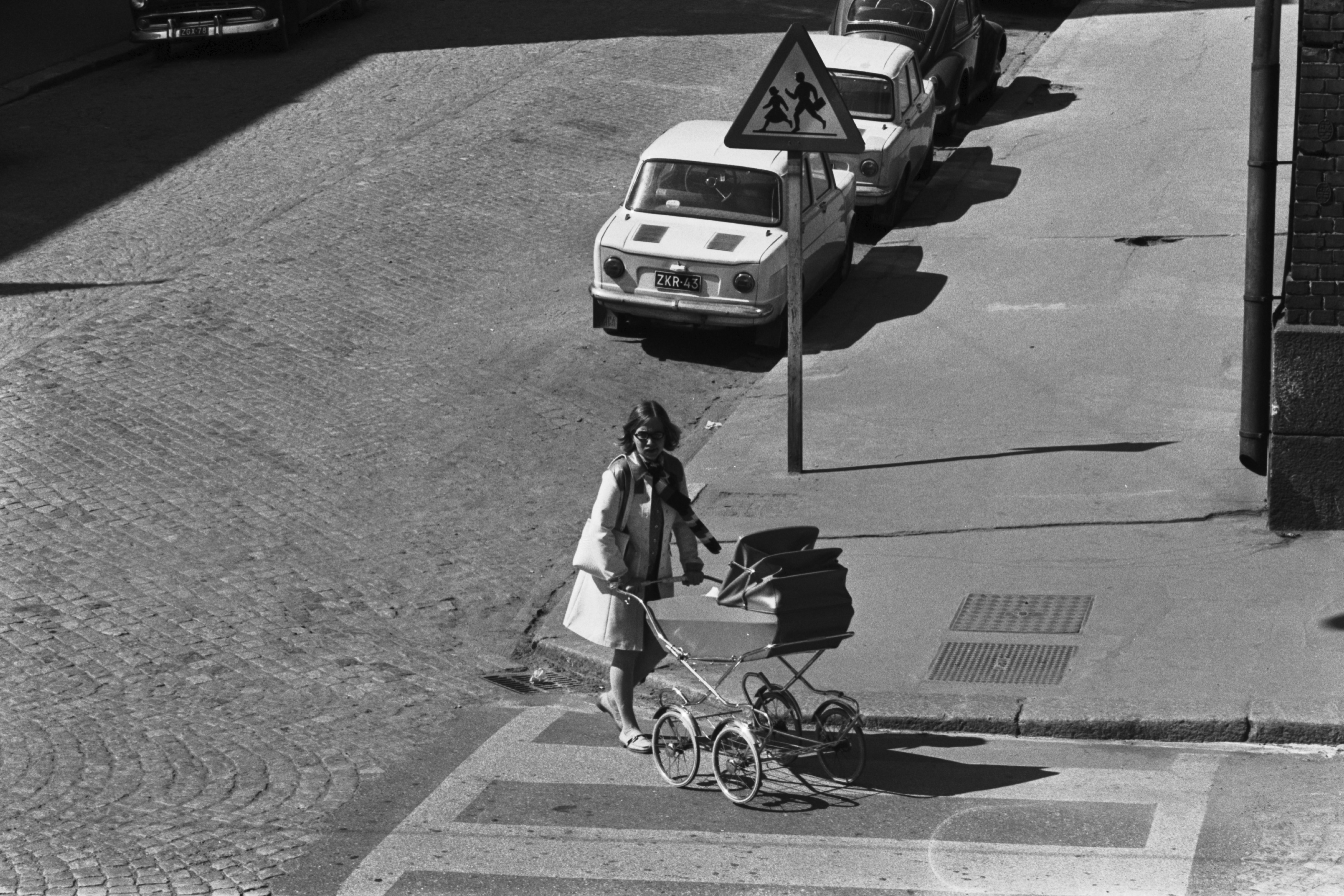 Porthaninkatu 7. Lastenvaunuja työntävä nainen ylittämässä katua Porthaninkadun ja Neljännen linjan risteyksessä, jossa lapsista varoittava likennemerkki.