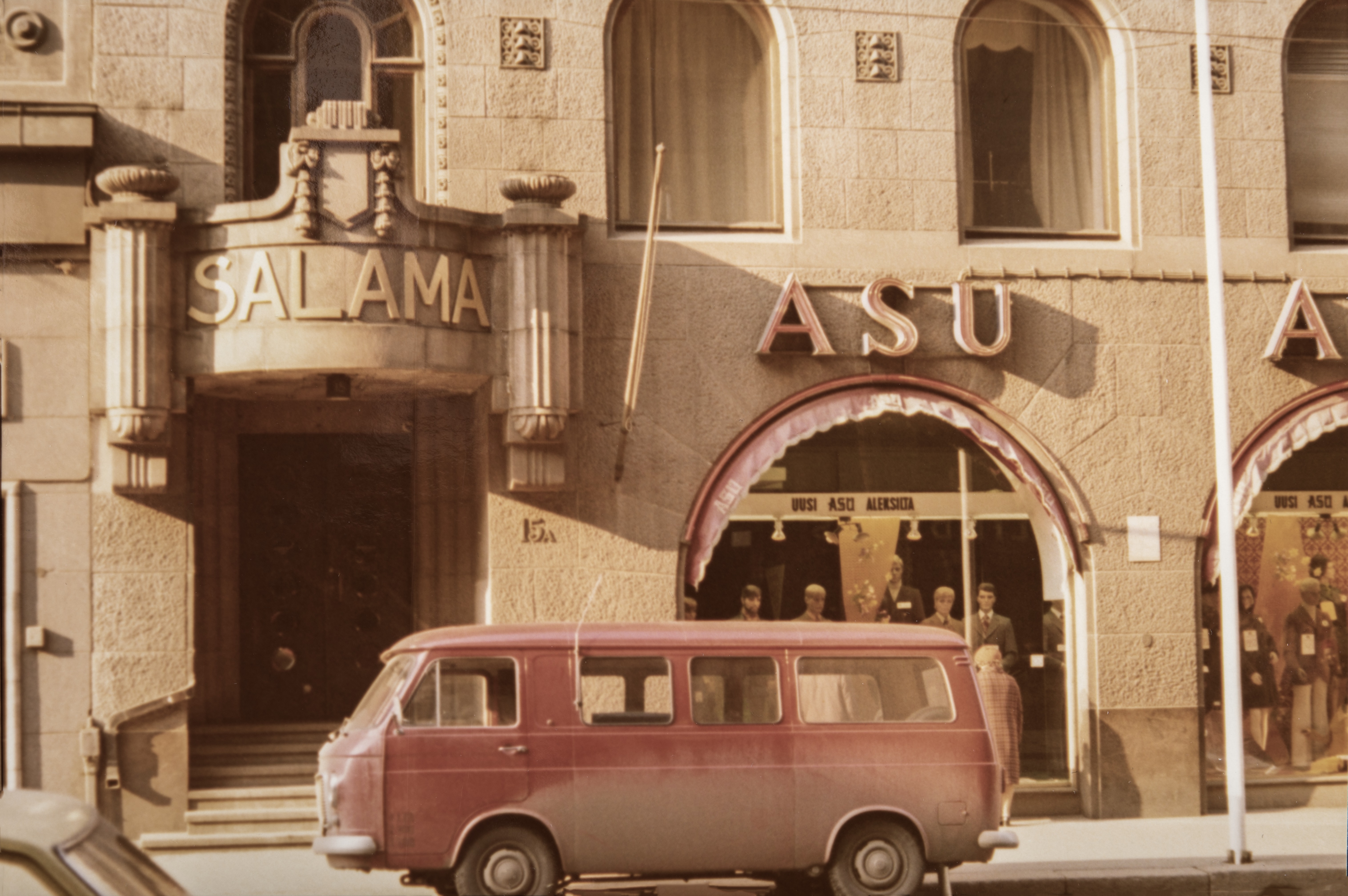 Salaman talo ja 1. kerroksen liikehuoneistoja. Kahdessa alimmassa kerroksessa on segmenttikaari-ikkunat. Julkisivun kummassakin reunassa on sisäänkäynti, ja näiden sivusisäänkäyntien yläpuolella lukee teksti Salama vakuutusyhtiö Salaman mukaan. Lisäksi näiden sisäänkäyntien yläpuolella on pienet parvekkeet. Liikehuoneiston vaatekaupan nimi Asu on kirjoitettu valokirjaimin jokaiseen kolmeen segmenttikaareen. Punainen pakettiauto on parkkeerattu vaatekaupan eteen sointuen vaatekaupan punaisiin valokiurjaimiin ja markiiseihin. Airam Electric Oy Ab:n  kuvamateriaalia.