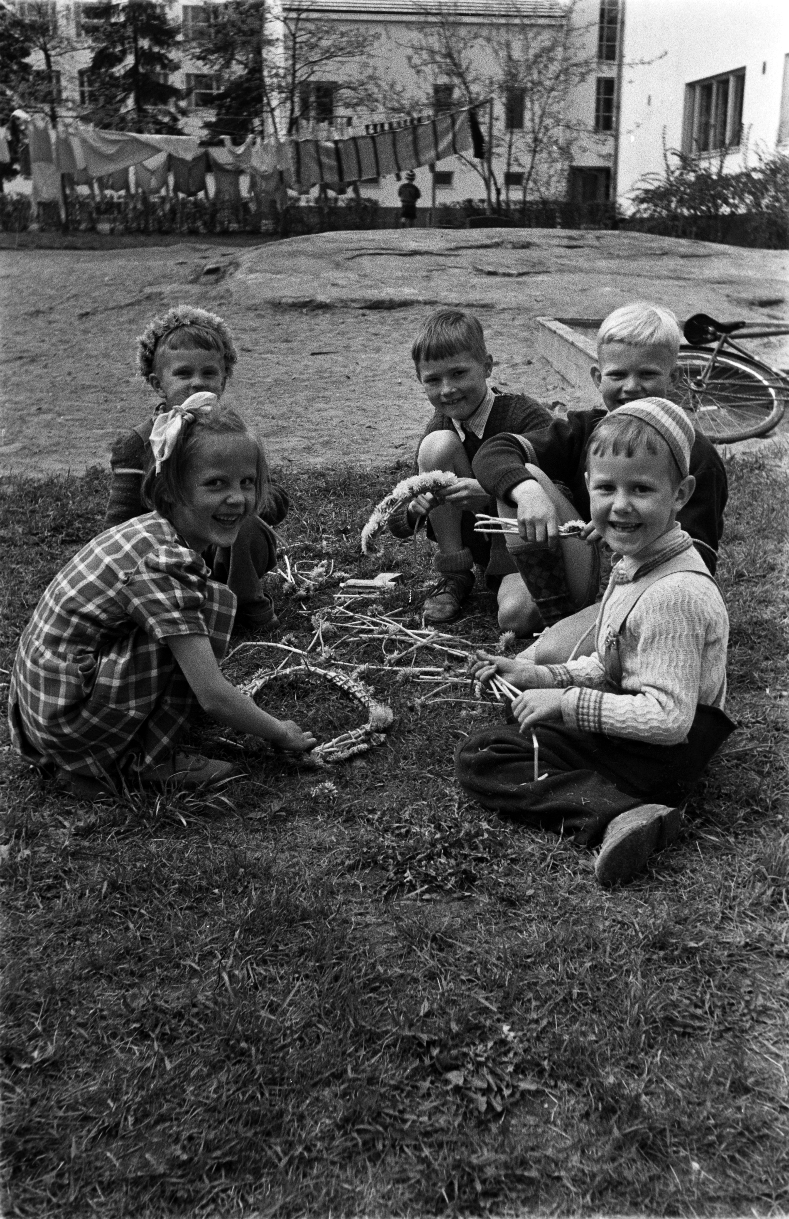 Koskelantie 40. Lapsia kokoamassa seppeleitä kukista Olympiakylän kerrostalon pihalla.