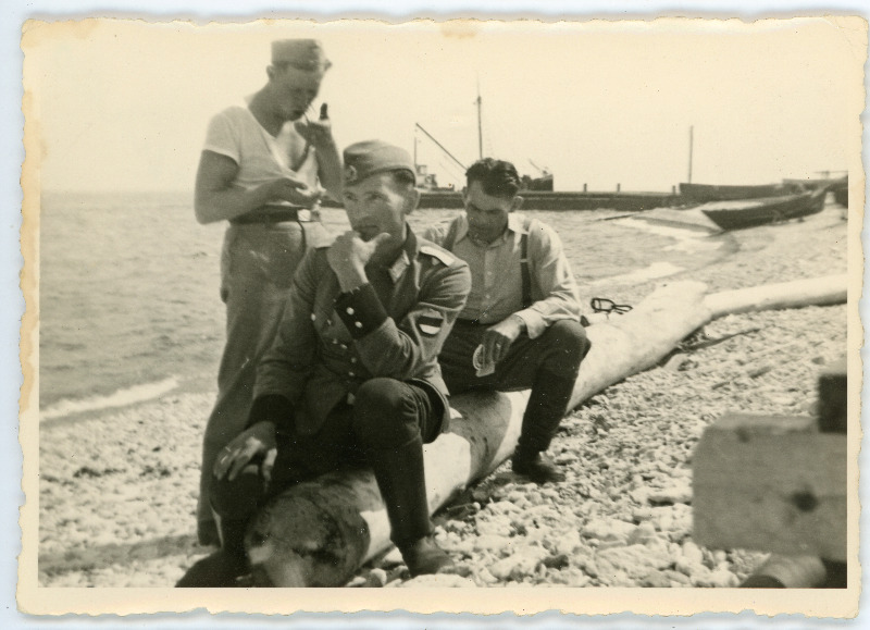 Eesti Leegioni sõdurid Pakri saare rannas palgil istumas, üks nendest mundris ja eraldusmärkidega