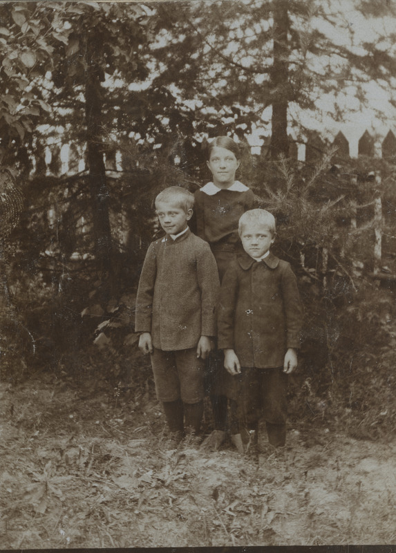 Kaks poissi ja üks tüdruk aia juures seismas