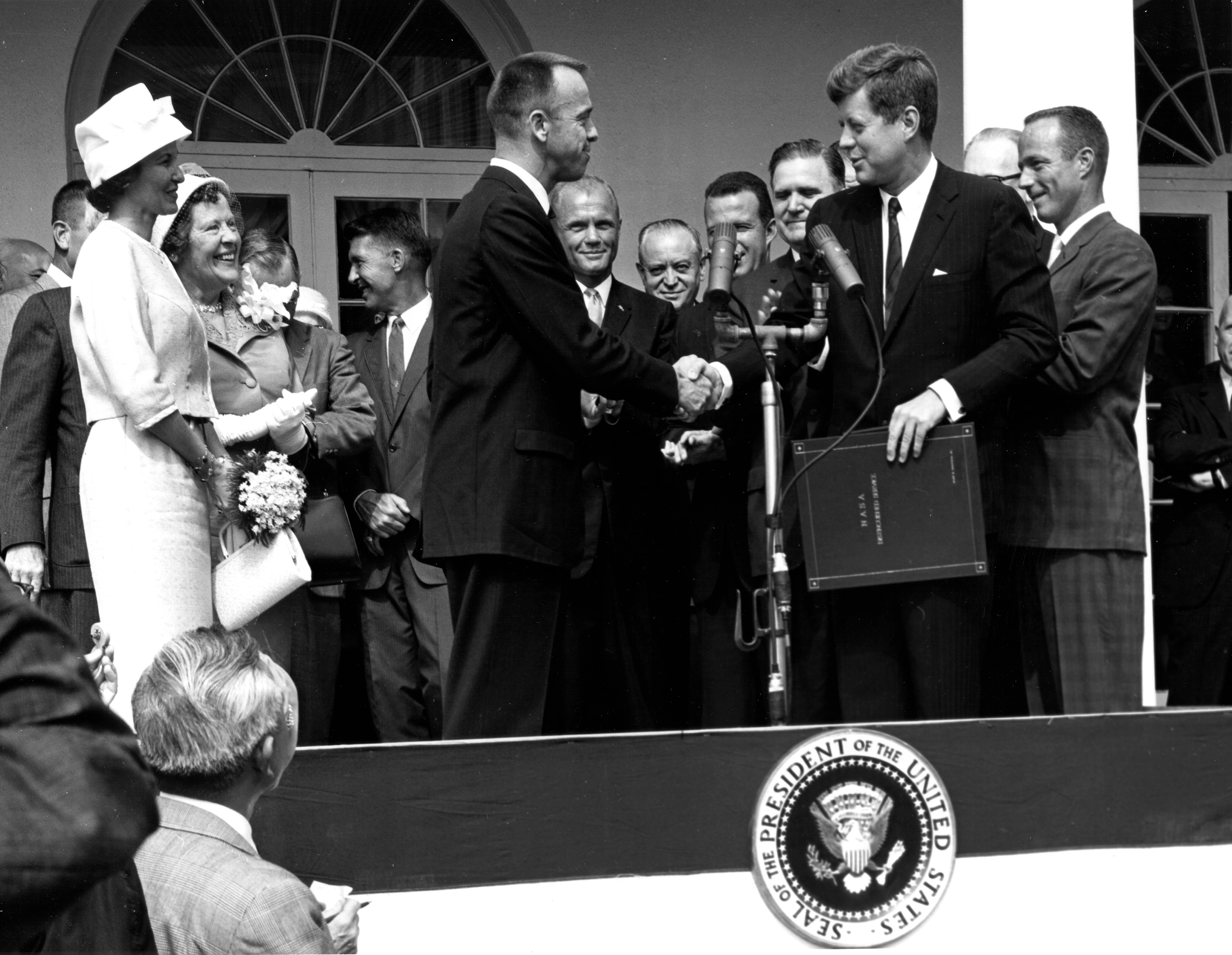 Kennedy and Shepard in Washington D.C. - GPN-2000-001659 - President John F. Kennedy congratulates astronaut Alan B. Shepard, Jr., the first American in space, on his historic May 5th, 1961 ride in the Freedom 7 spacecraft and presents him with the NASA Distinguished Service Award. The ceremony took place on the White House lawn. Shepard's wife, Louise (left in white dress and hat), and his mother were in attendance as well as the other six Mercury astronauts and NASA officals, some visible in the background.