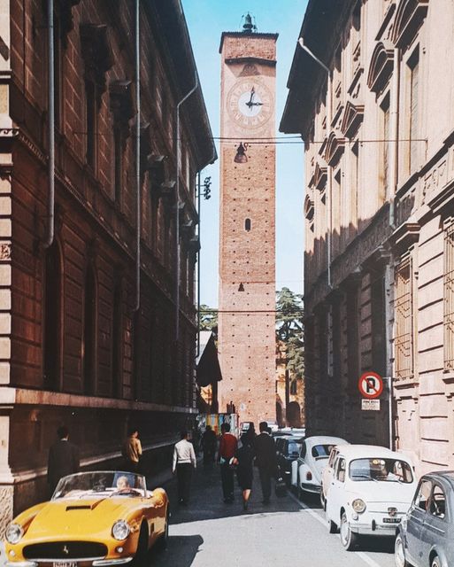 1966 Pavia Ferrari 250 Cal Spyder 1077GT - Torre dell'orologia ("clock tower")  in Pavia, one of the famous Tre torri on the Piazza Leonardo da Vinci. The small street may be Via Maria Corti (says Google Maps), picture taken from Via Mentana. We see a yellow Ferrari. It is a Ferrari 250 GT California SWB Spyder, I think. It was made 1960 to 63. It has a split front bumper, which must be very rare. License plate is italian, wonder if there is a "FI" in it (indicationg Firenze, which is not that far away from Pavia)  Guessing 5 May 1963. Update: Wrong. It is 1966 and 1077GT!
