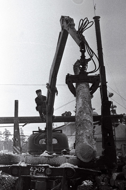 Läänemaa Metsamajandi tööline Jaak Järv tõstab mehhanismiga palgi autolt transportööri kõrvale.