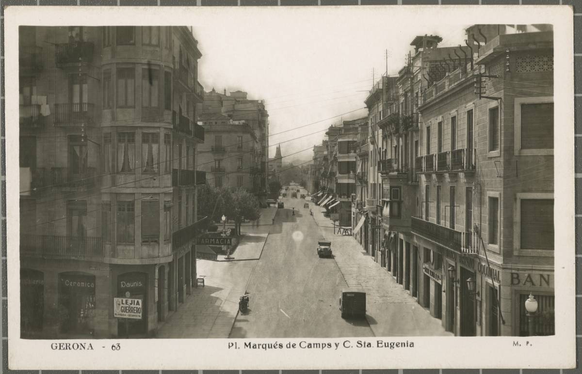 63 GERONA. Pl. Marquis de Camps y C. Eugenia - View of the Santa Eugenia road at the height of Plaza Marqués de Campos, with different cars and cars circulating First on the left the Casa Daunis de venta de cristallería y ceramics and next to it, a pharmacy On the right, Banco Hispano Colonial Corominas house. In the background Tejedor house known as the Puncha