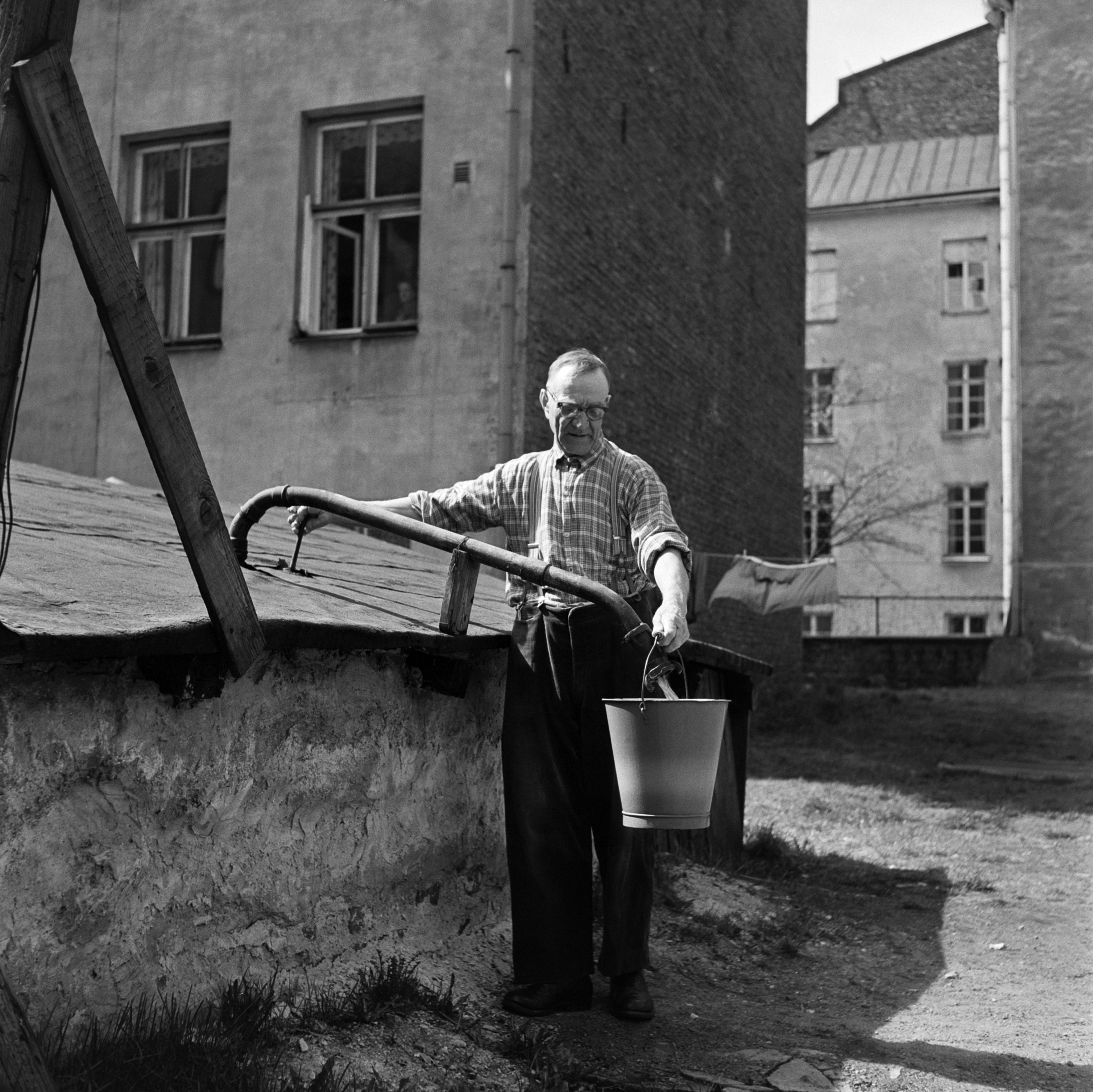 Mies hakee vettä yhteisestä vesipostista pihalla